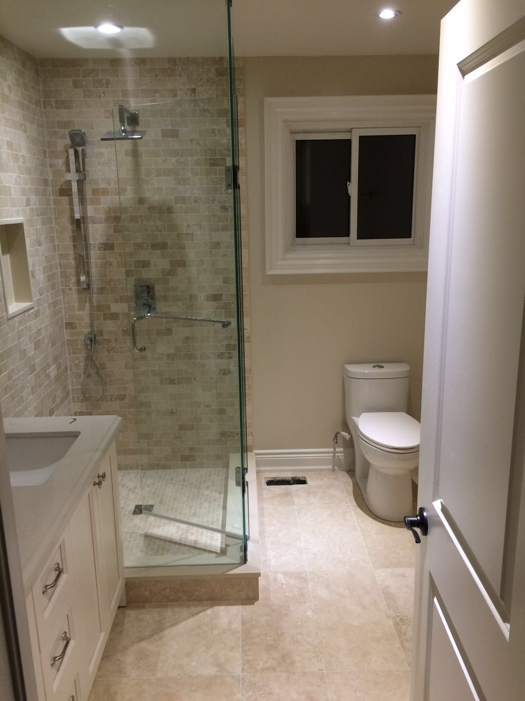 This Toronto bathroom renovation features a clean and functional layout with a walk-in glass shower, custom tiled shower walls, and a modern vanity with integrated storage. Neutral tile flooring and recessed lighting enhance brightness and usability, while the frameless glass enclosure creates a more open feel. The upgraded design improves daily comfort, durability, and visual appeal, making it a practical and modern bathroom solution for Toronto homes.