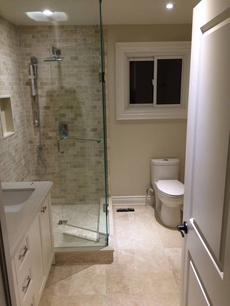 This Toronto bathroom renovation features a clean and functional layout with a walk-in glass shower, custom tiled shower walls, and a modern vanity with integrated storage. Neutral tile flooring and recessed lighting enhance brightness and usability, while the frameless glass enclosure creates a more open feel. The upgraded design improves daily comfort, durability, and visual appeal, making it a practical and modern bathroom solution for Toronto homes.