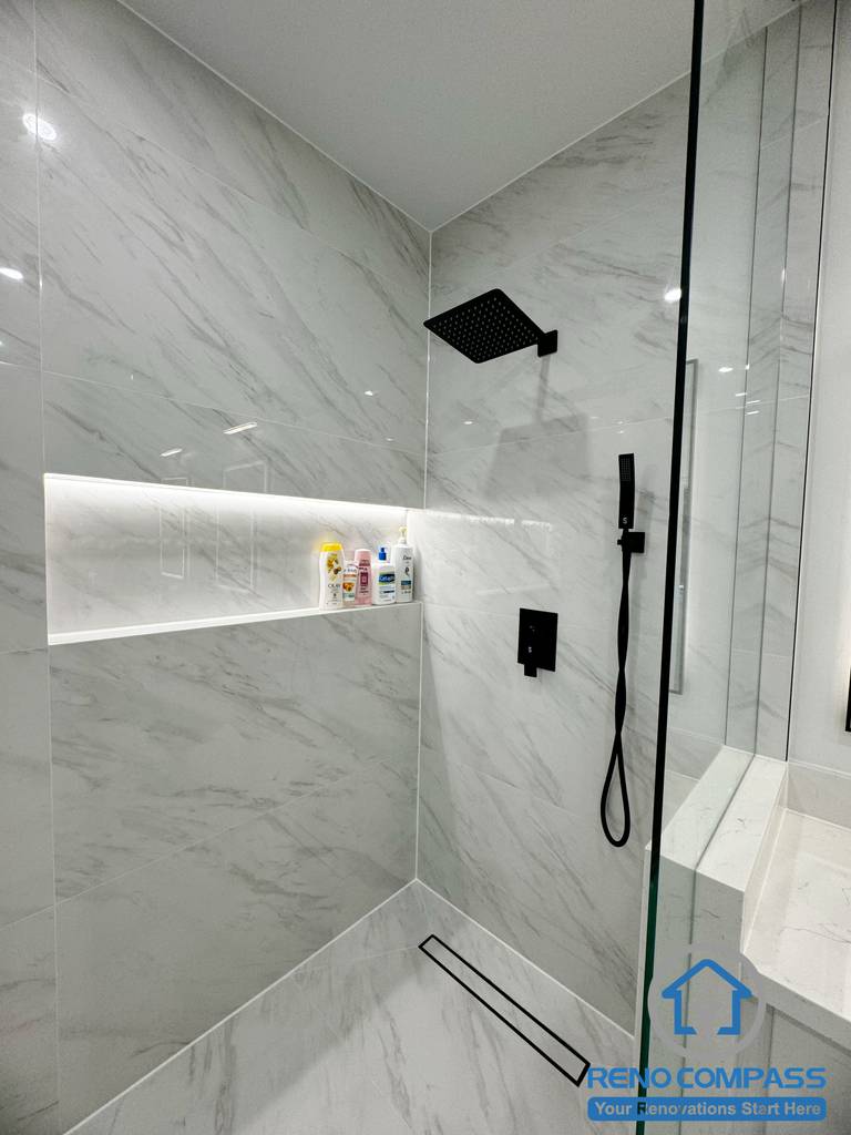 This Vaughan bathroom renovation highlights a frameless glass shower finished with large-format marble-look tiles and a built-in LED-lit wall niche for storage. Matte black shower fixtures and a linear floor drain create a sleek, modern aesthetic while improving functionality and water drainage. Completed by a professional Toronto Renovation Company, this shower design combines minimalist style with durable, high-end materials for long-term performance.