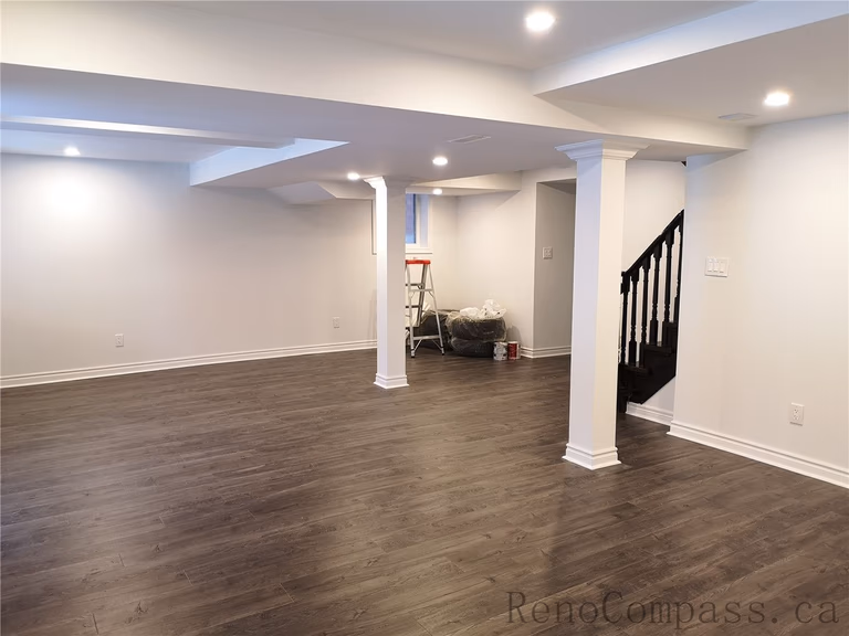 This Richmond Hill basement renovation showcases a spacious open-concept layout with newly installed dark wood flooring, pot lights, and clean modern finishes. Structural columns were integrated seamlessly into the design to maintain an open and functional living space. The upgraded lighting and neutral wall tones create a warm and inviting basement environment ideal for family use or entertainment. Completed by a professional Toronto renovation company, Reno Compass Inc., this finished basement delivers both comfort and contemporary style.