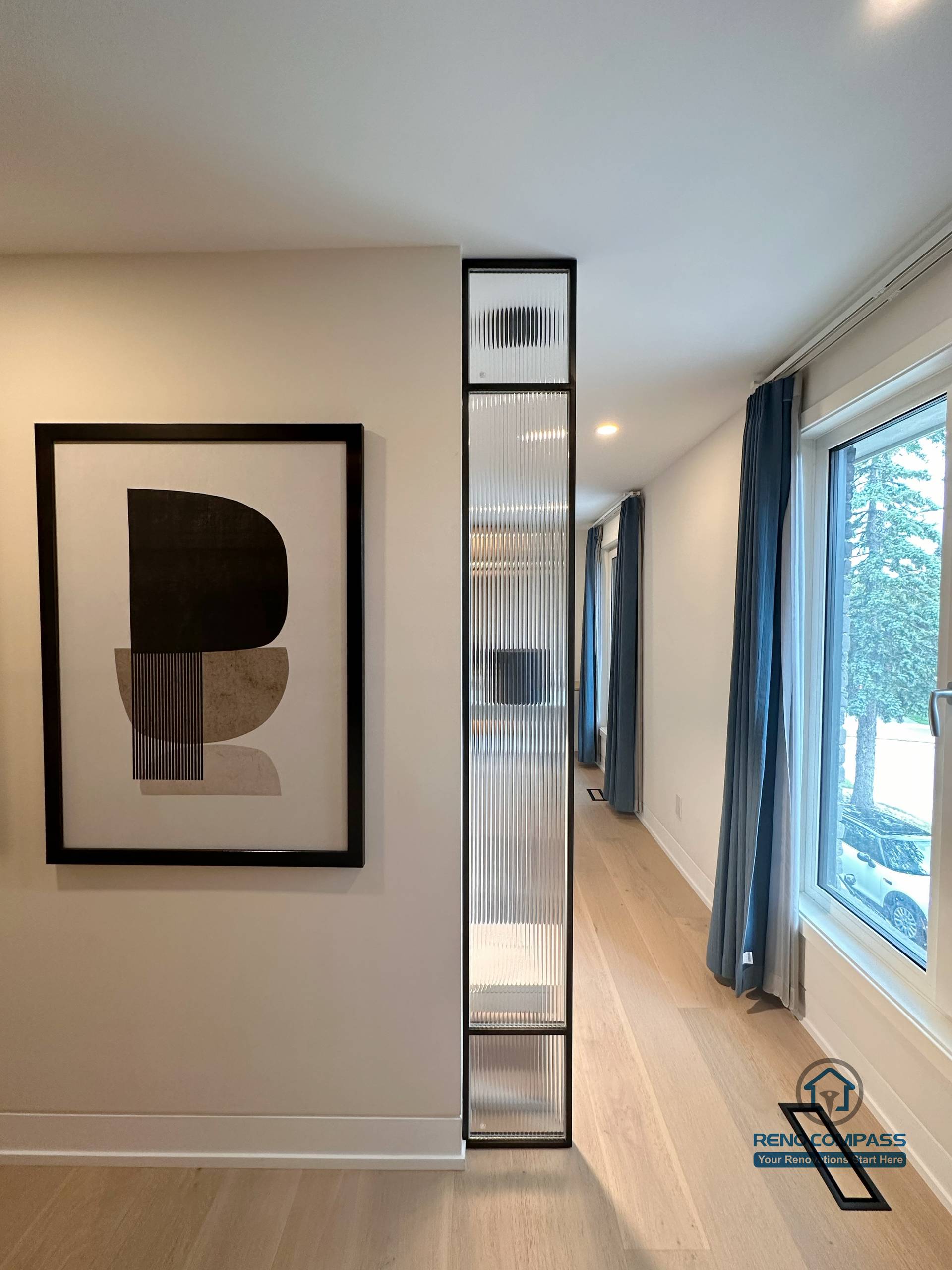 This Toronto interior renovation highlights a clean hallway design with light hardwood flooring, a slim glass partition feature, and large windows that enhance natural light. The seamless flooring installation and minimalist detailing create visual continuity and depth, showcasing refined craftsmanship ideal for modern Toronto home renovations.