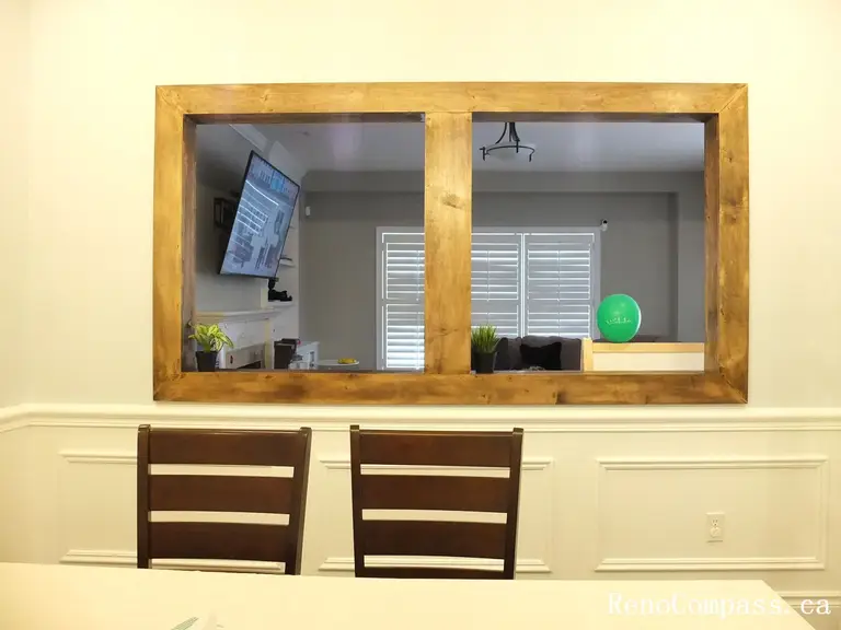 Interior renovation in Newmarket featuring a custom framed viewing window that connects the dining room and living area. Designed with detailed wall panel molding and hardwood flooring, this thoughtful upgrade was completed by a professional Toronto Renovation Company to enhance openness and visual continuity.