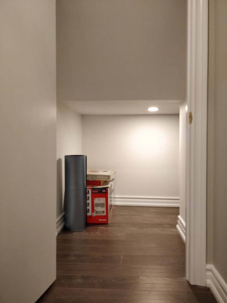 This image showcases a finished basement hallway and lower-level storage area from a Scarborough basement renovation project. The space features newly installed hardwood flooring, smooth neutral wall finishes, recessed pot lighting, and clean baseboard detailing for a polished and cohesive look. The improved layout enhances accessibility while maximizing usable square footage in the basement. Completed by Reno Compass Inc., this renovation reflects practical space optimization combined with modern interior finishes for long-term functionality.