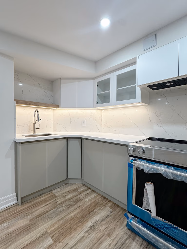 This image focuses on a detailed view of the basement kitchen renovation in Pickering, highlighting the corner layout and functional workspace design. Custom cabinetry, integrated under-cabinet lighting, and a continuous countertop create a practical and efficient kitchen setup suitable for everyday use. The corner sink placement improves workflow while maintaining a clean and organized appearance. Neutral finishes and consistent flooring allow the kitchen area to blend seamlessly into the surrounding basement living space, supporting a cohesive and flexible lower-level layout.
Location: Pickering · Toronto Contractor: Reno Compass