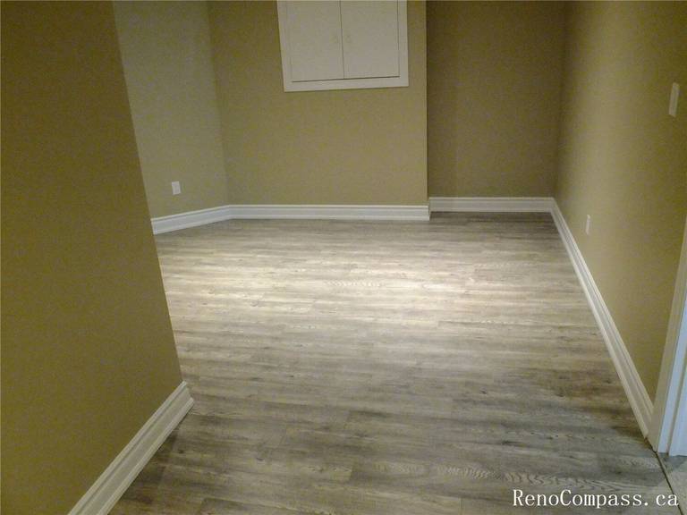 A bright, expansive basement transformation in Ajax, Ontario. This open-concept living space features energy-efficient recessed pot lighting, modern grey vinyl plank flooring, and a neutral color palette. Expertly designed for a home theater, family play area, or exercise room.