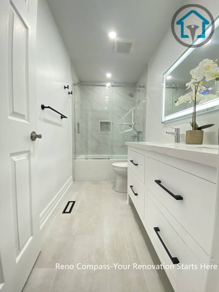 This Pickering bathroom renovation highlights a streamlined layout designed to maximize visual length and openness. A custom vanity with matte black hardware runs along one side, paired with light-toned flooring to enhance brightness. The frameless glass shower enclosure and marble-style wall tiles create a seamless transition, giving the bathroom a clean, modern, and well-balanced feel.