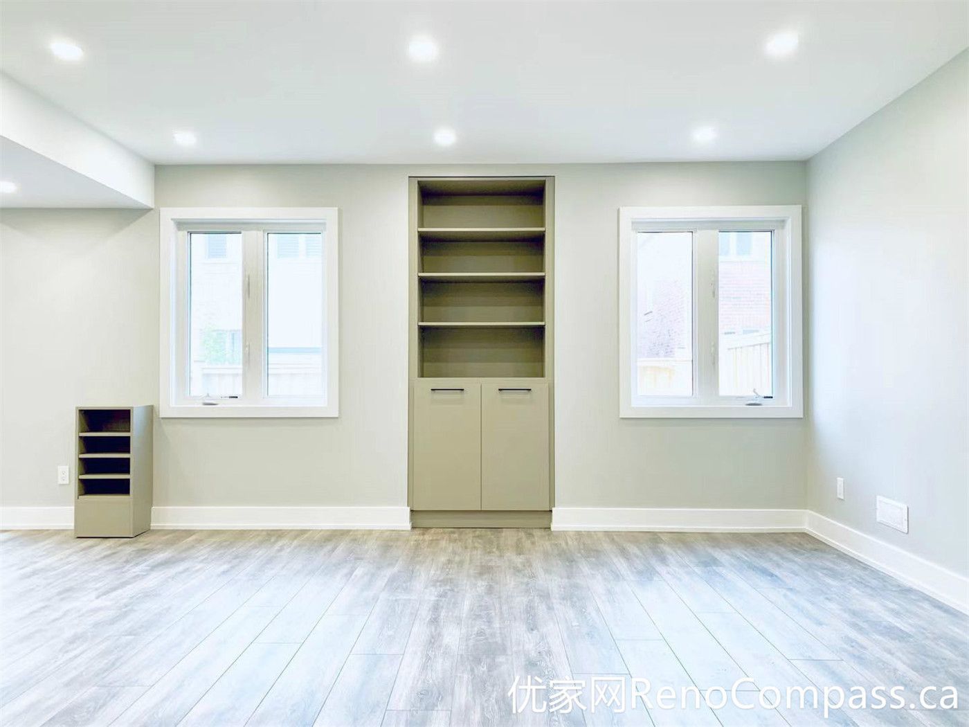 This Markham basement renovation features a bright open living area with integrated built-in shelving and durable wood-look flooring. The symmetrical window layout enhances natural light, while the custom storage solution adds both practicality and a clean, organized aesthetic.
