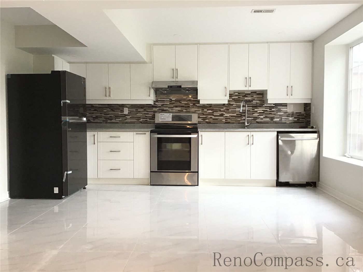 Completed basement kitchen renovation in Whitby featuring full-height white cabinetry, stainless steel appliances, mosaic tile backsplash, and bright polished flooring. The open layout maximizes natural light and creates a clean, contemporary secondary living space ideal for rental or extended family use. Delivered by a professional Toronto renovation company, this Whitby basement project demonstrates efficient space planning and high-quality finishing.