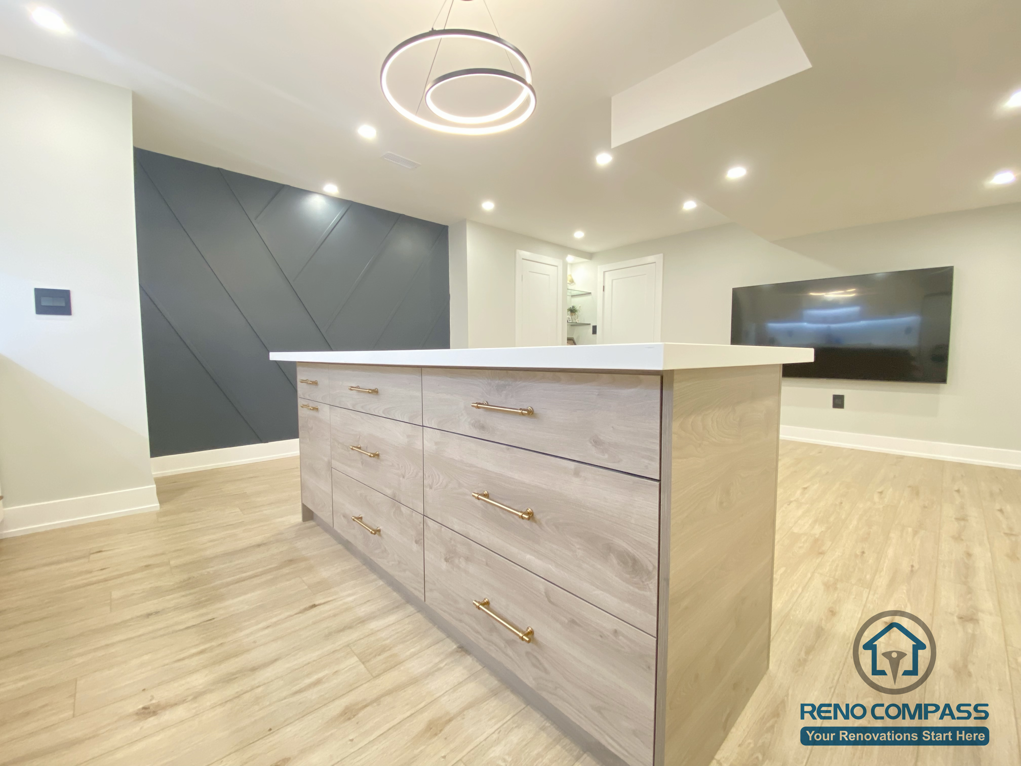 This Aurora basement renovation features a custom-built kitchen island with wood-tone cabinetry, modern hardware, and a sleek white countertop. The space is enhanced by contemporary pendant lighting, recessed ceiling lights, and an open-concept layout that connects the kitchen and entertainment areas seamlessly. Completed by a Toronto renovation company, this basement renovation highlights functional design, clean lines, and refined modern finishes.
