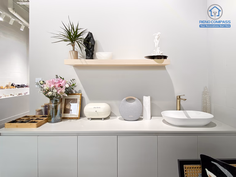 This image features a custom cabinetry and utility counter designed as part of a crystal shop renovation in Markham. The space includes built-in storage cabinets, a minimalist countertop with integrated sink, floating display shelf, and carefully styled decorative elements. Soft neutral finishes and functional layout support daily retail operations while maintaining a calm, curated aesthetic. As a Toronto renovation company, Reno Compass delivers retail renovation solutions that combine practical workspace design with refined visual presentation.