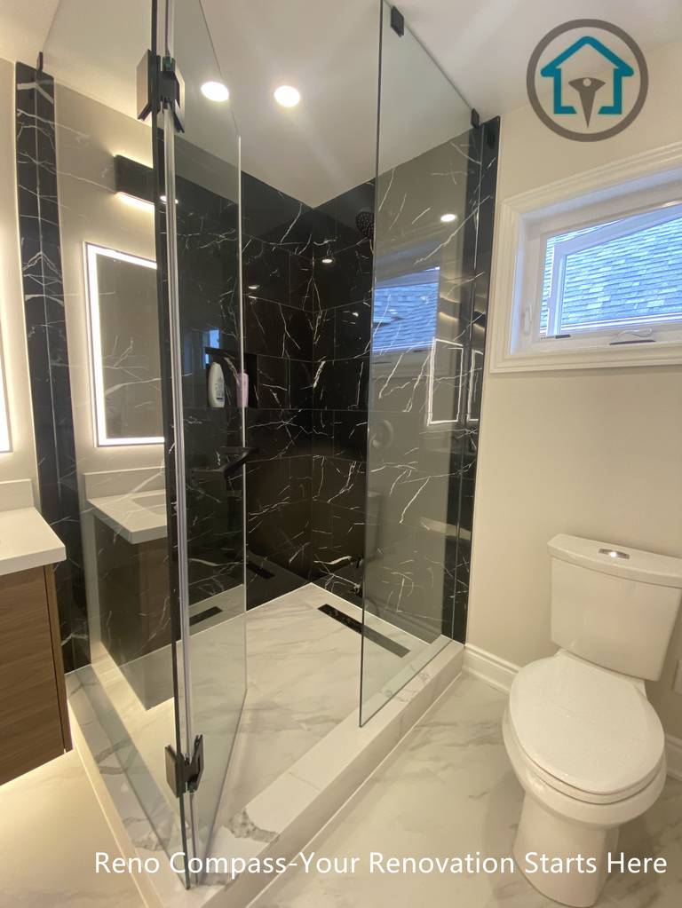 This Richmond Hill bathroom renovation features a modern frameless glass walk-in shower with elegant black marble wall tiles and sleek chrome fixtures. The upgraded layout improves space efficiency after converting one bathroom into two, adding functionality and value to the home. Bright LED mirror lighting, marble-style flooring, and a clean contemporary design create a luxurious and practical bathroom completed by a trusted Toronto renovation company.