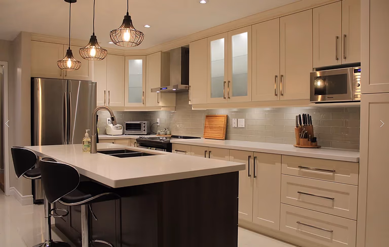 This Mississauga kitchen renovation features custom cream cabinetry, a large quartz island, modern pendant lighting, and upgraded backsplash design. Completed by a professional Toronto renovation company, the project focuses on improving functionality, storage, and modern aesthetics. The spacious island with built-in sink and seating enhances daily use and entertaining, while new lighting and finishes create a warm, elegant atmosphere. Ideal for homeowners in Mississauga seeking a stylish and practical kitchen upgrade with high-quality craftsmanship and thoughtful layout planning.