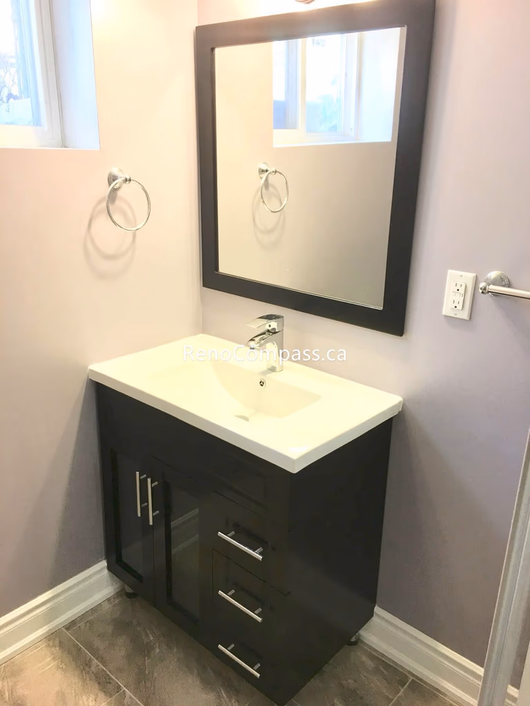 This Toronto basement renovation features a modern bathroom vanity with quartz countertop, under-mount sink, and sleek black cabinet design. The large framed mirror and neutral wall tones create a bright and elegant space, while durable tile flooring ensures long-term performance. Completed by a trusted Toronto renovation company, this basement bathroom upgrade enhances functionality, storage, and contemporary home value.