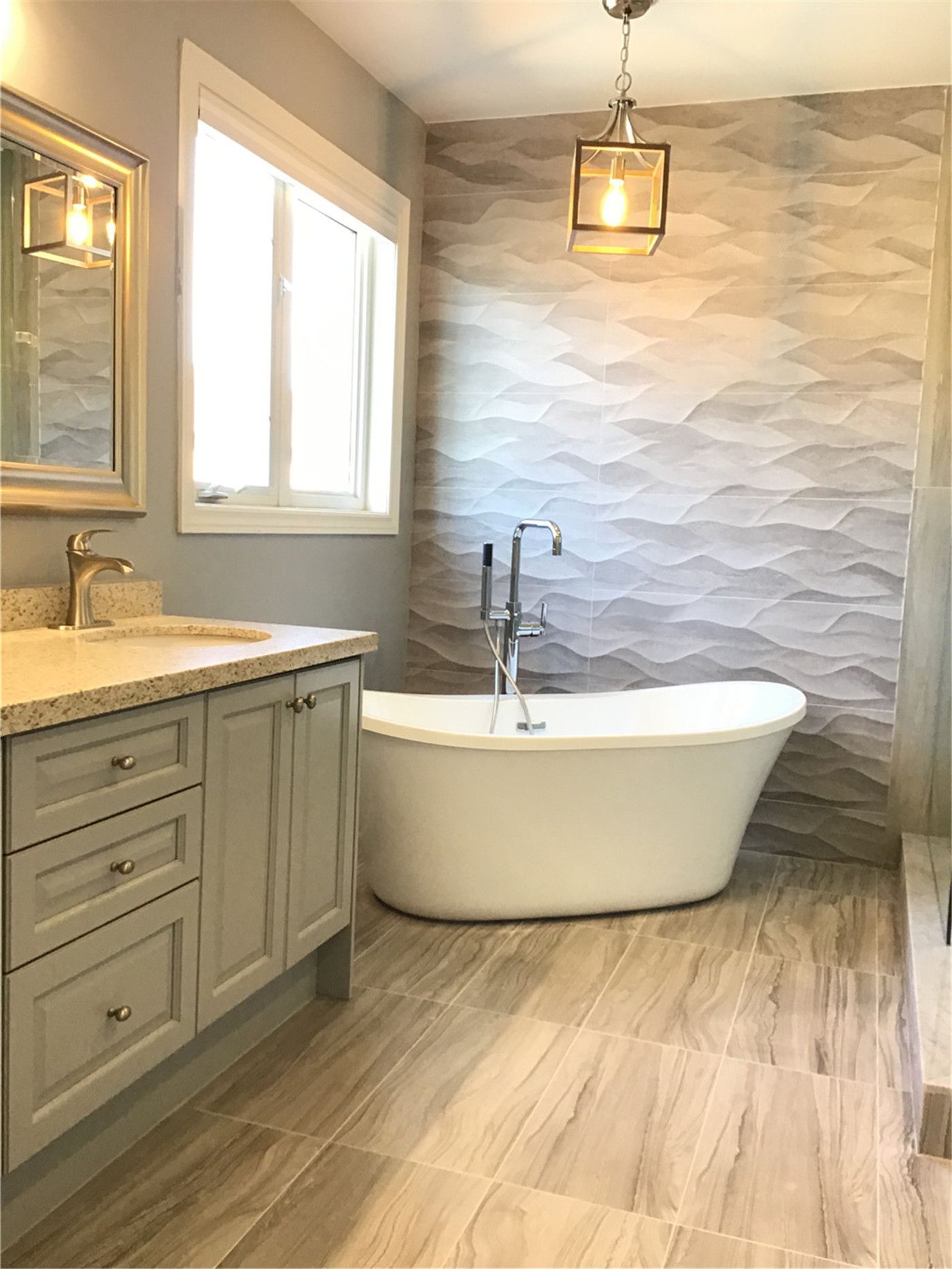 This Woodbridge bathroom renovation features a modern freestanding bathtub paired with a textured 3D feature wall tile, creating a spa-like atmosphere. The space is completed with a grey vanity, quartz countertop, and warm lighting fixtures, offering a perfect balance of comfort, elegance, and functionality.
