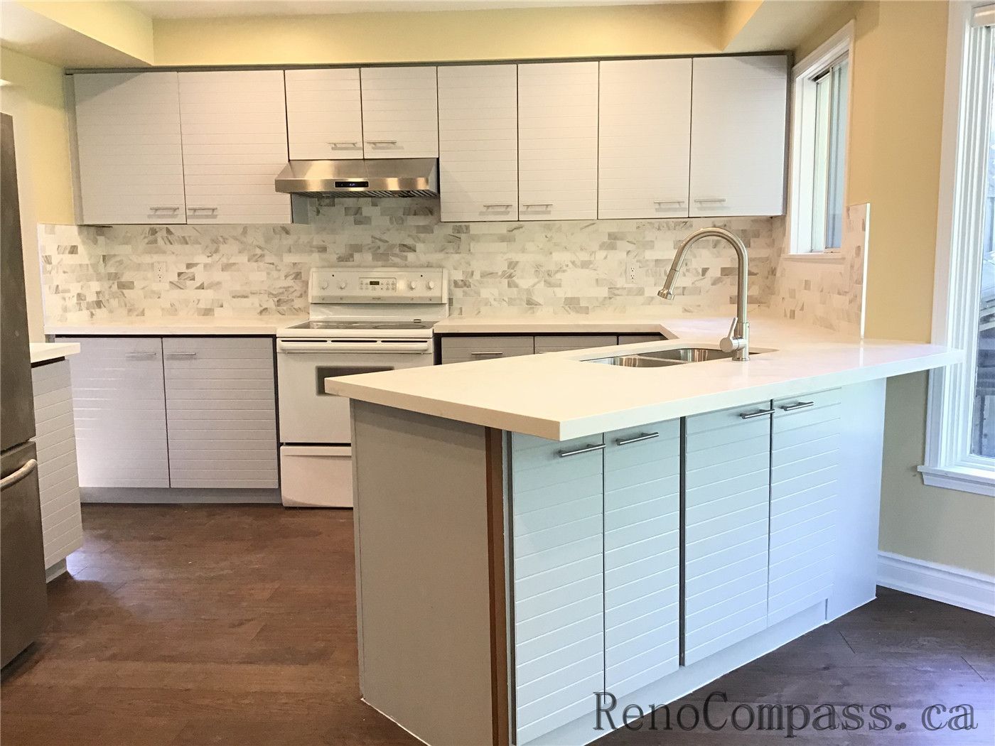 This image features a fully renovated kitchen in Richmond Hill, showcasing modern white cabinetry, a functional central island with sink, and a clean marble-style backsplash. The layout enhances both usability and visual brightness, creating a sleek and inviting cooking space.