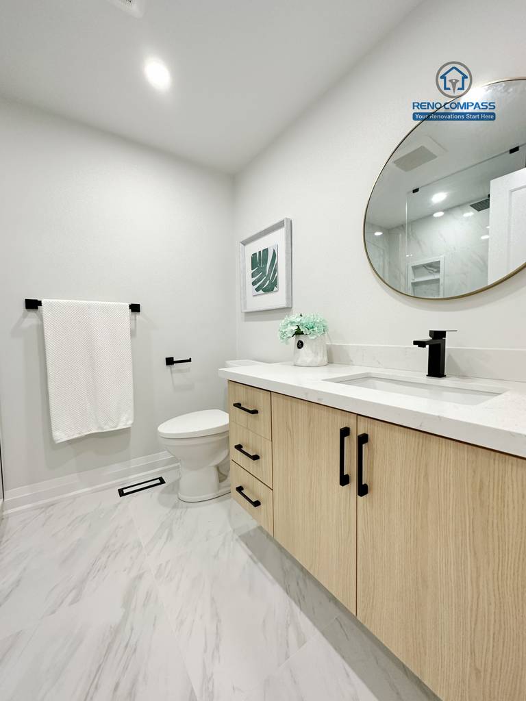 This Richmond Hill interior renovation showcases a modern bathroom vanity with natural wood cabinetry, quartz countertop, and a round mirror with black fixtures. The clean layout and neutral tones create a bright and functional powder room. Completed by a Toronto renovation company, the space balances practicality with contemporary style.