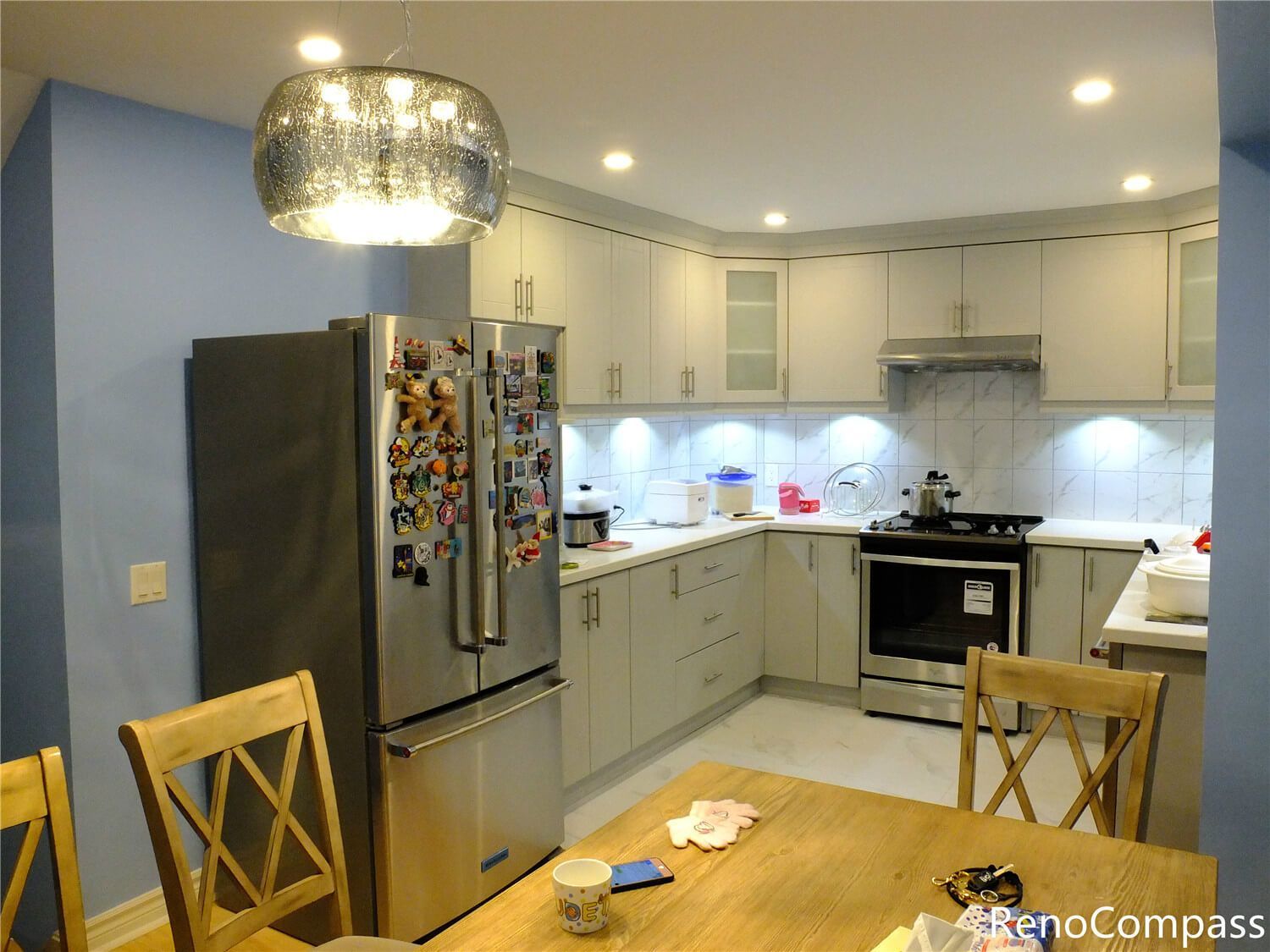 This Aurora kitchen renovation showcases a bright and functional kitchen layout featuring custom white cabinetry, stainless steel appliances, and a marble-pattern backsplash. Recessed ceiling lights and under-cabinet lighting enhance the overall brightness, while the open connection to the dining area creates a comfortable space for family gatherings. The updated kitchen combines modern finishes with practical storage solutions, reflecting the quality workmanship of Reno Compass Inc., a trusted Toronto renovation company serving Aurora and the Greater Toronto Area.