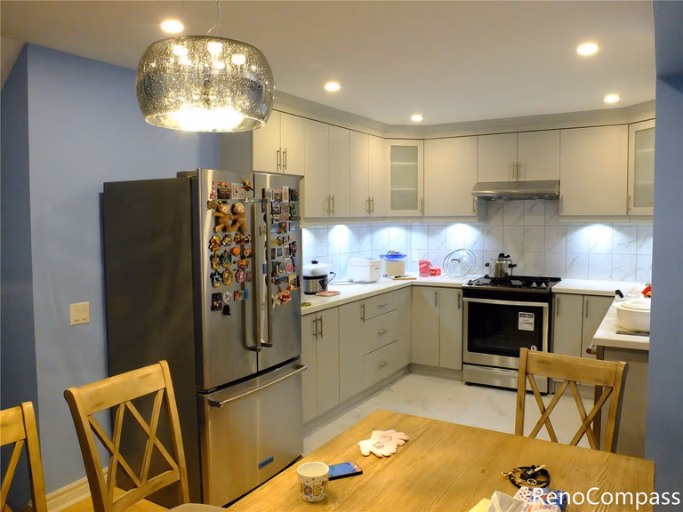 This Aurora kitchen renovation showcases a bright and functional kitchen layout featuring custom white cabinetry, stainless steel appliances, and a marble-pattern backsplash. Recessed ceiling lights and under-cabinet lighting enhance the overall brightness, while the open connection to the dining area creates a comfortable space for family gatherings. The updated kitchen combines modern finishes with practical storage solutions, reflecting the quality workmanship of Reno Compass Inc., a trusted Toronto renovation company serving Aurora and the Greater Toronto Area.