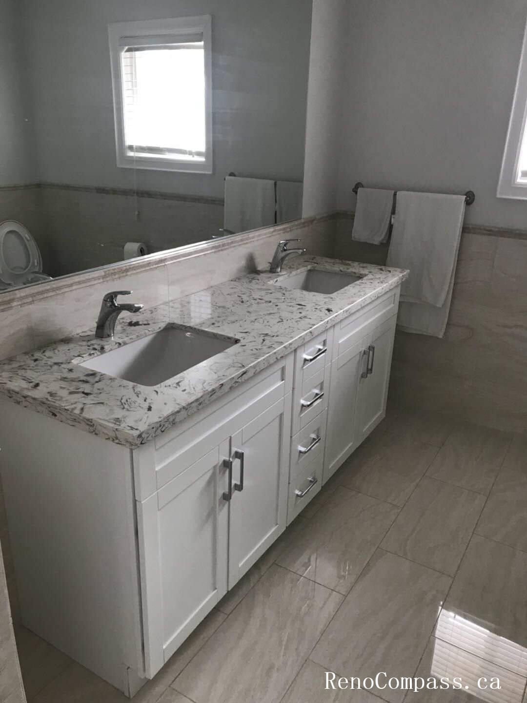 This Markham interior renovation features a modern bathroom upgrade highlighted by a spacious double-sink vanity with a premium quartz countertop. The custom white cabinetry provides ample storage while maintaining a clean and timeless aesthetic. Undermount sinks paired with sleek chrome faucets enhance functionality and durability. Large-format porcelain floor tiles complement the neutral wall tones, creating a bright and cohesive design. The full-width mirror expands the visual space and reflects natural light for a more open atmosphere. This bathroom renovation demonstrates Reno Compass’ attention to detail and commitment to delivering high-quality interior renovation services in Markham and the Greater Toronto Area.