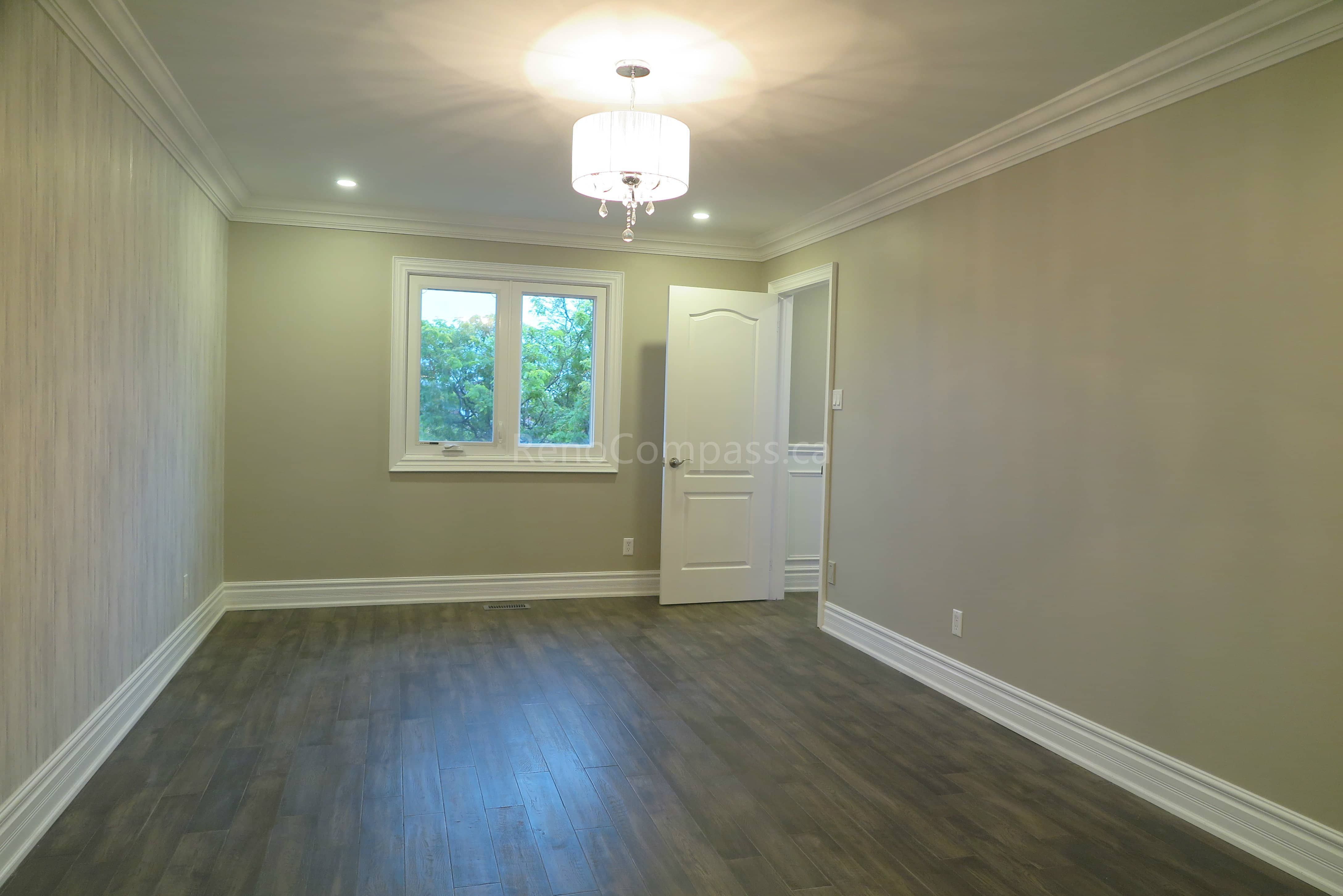 This Markham interior renovation features a bright and modern bedroom with newly installed hardwood flooring, neutral wall finishes, and elegant crown molding details. A contemporary ceiling light fixture and recessed lighting enhance the overall ambiance, while large windows provide natural light for a comfortable living environment. Completed by Reno Compass, a professional renovation contractor specializing in full interior renovations and custom finishing services across Markham and the Greater Toronto Area.