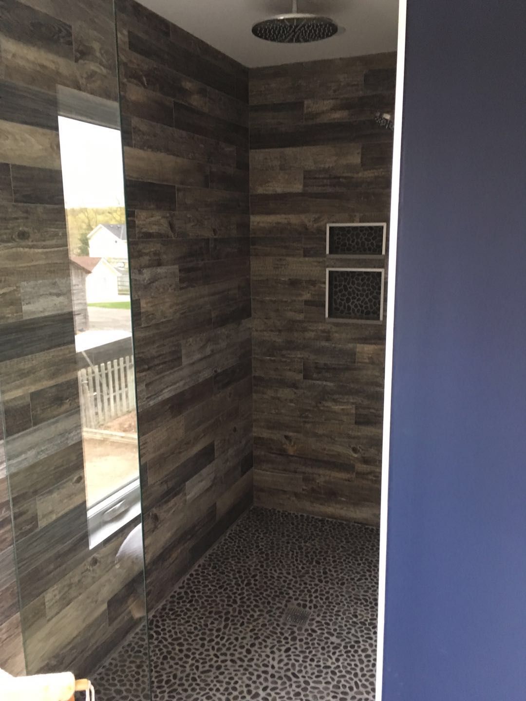 This Toronto bathroom renovation features a custom walk-in shower designed with textured wood-look wall tiles and pebble stone flooring for a natural, spa-inspired feel. The built-in shower niches provide convenient storage while maintaining a clean and seamless look. A large vertical window allows natural light to brighten the space, enhancing the modern and relaxing atmosphere. Completed by a professional Toronto renovation company, this shower upgrade combines durability, functionality, and contemporary design.