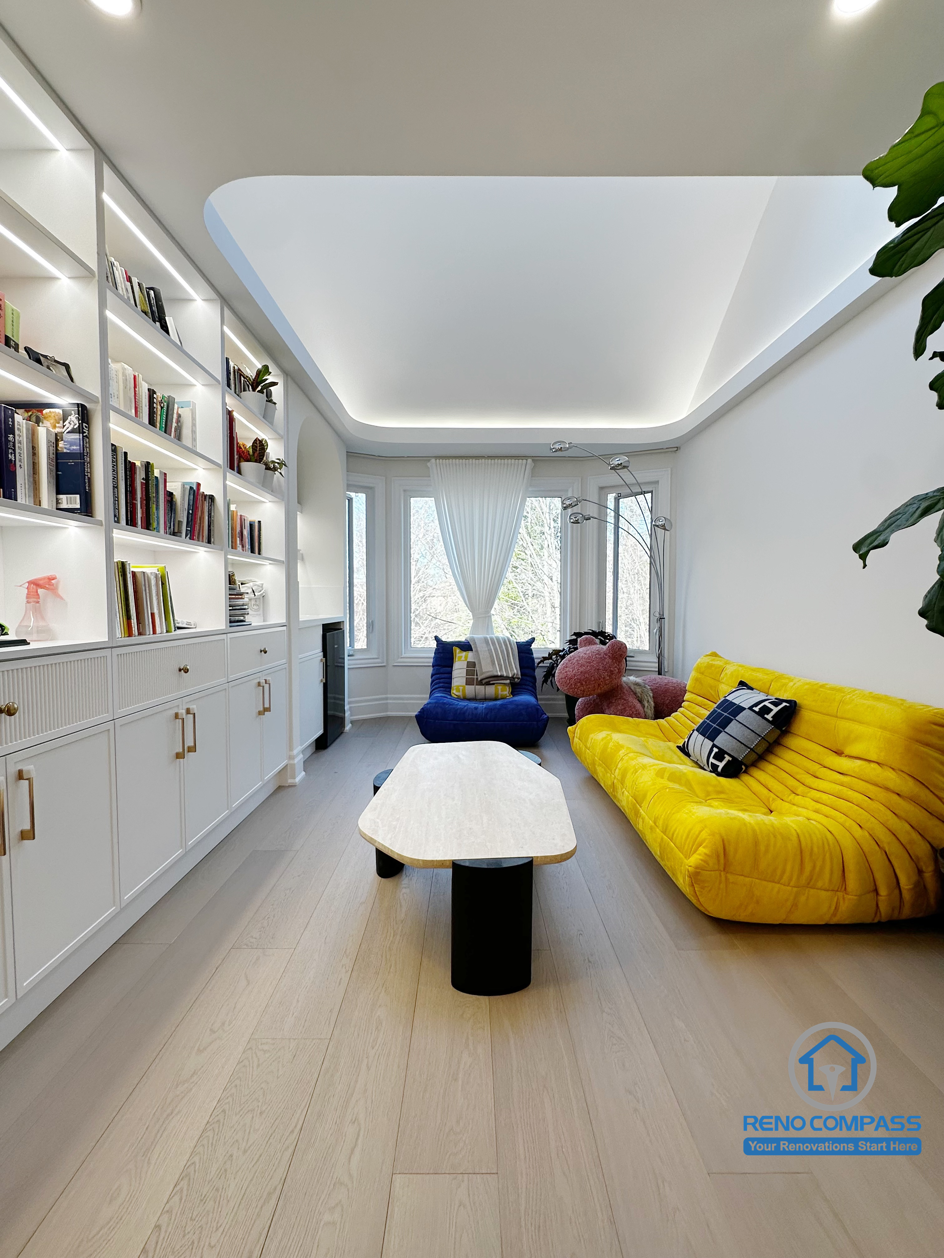 This area of the Markham interior renovation was designed as a calm, functional lounge that combines custom storage with everyday comfort. Full-height built-in shelving along one wall provides organized space for books and personal items while maintaining a clean, integrated appearance within the room.

The ceiling design features recessed lighting and soft indirect illumination, creating an even and inviting atmosphere without visual clutter. Light wood flooring helps balance the white cabinetry and bright furnishings, ensuring the space feels warm rather than overly minimal.

Designed for reading, relaxation, and quiet family time, this lounge area reflects a thoughtful approach to interior planning—where storage, lighting, and comfort work together to support daily living.