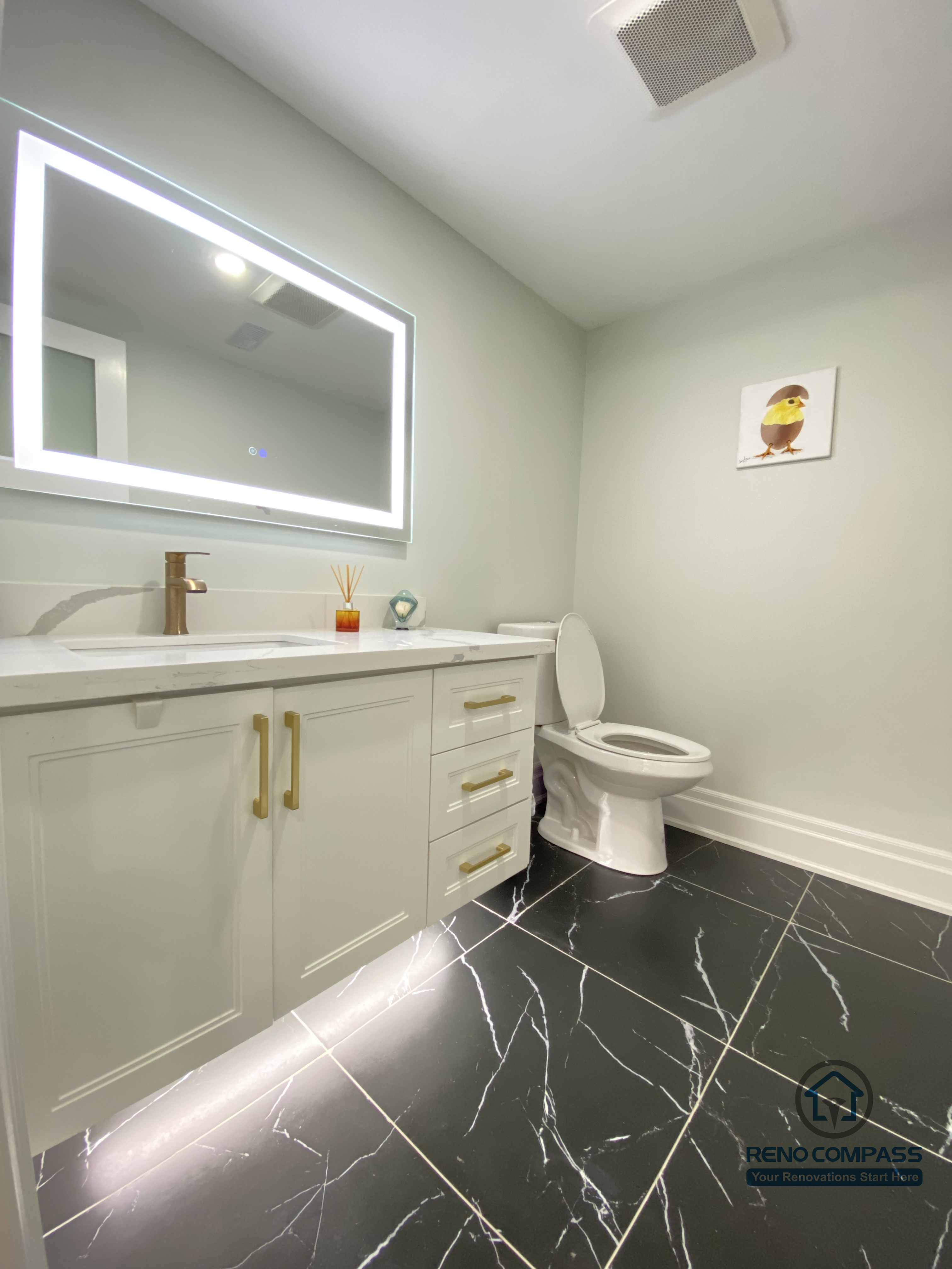 This Oakville basement renovation includes a modern bathroom designed with clean lines and practical comfort. The space features a custom vanity with integrated storage, a sleek LED backlit mirror, and black marble-style floor tiles that add contrast and visual depth. Soft neutral wall tones and efficient ventilation ensure a bright, fresh atmosphere suitable for everyday use. As a professional Toronto renovation company, Reno Compass delivers basement bathrooms that balance durability, lighting design, and refined finishes for long-term functionality and style.