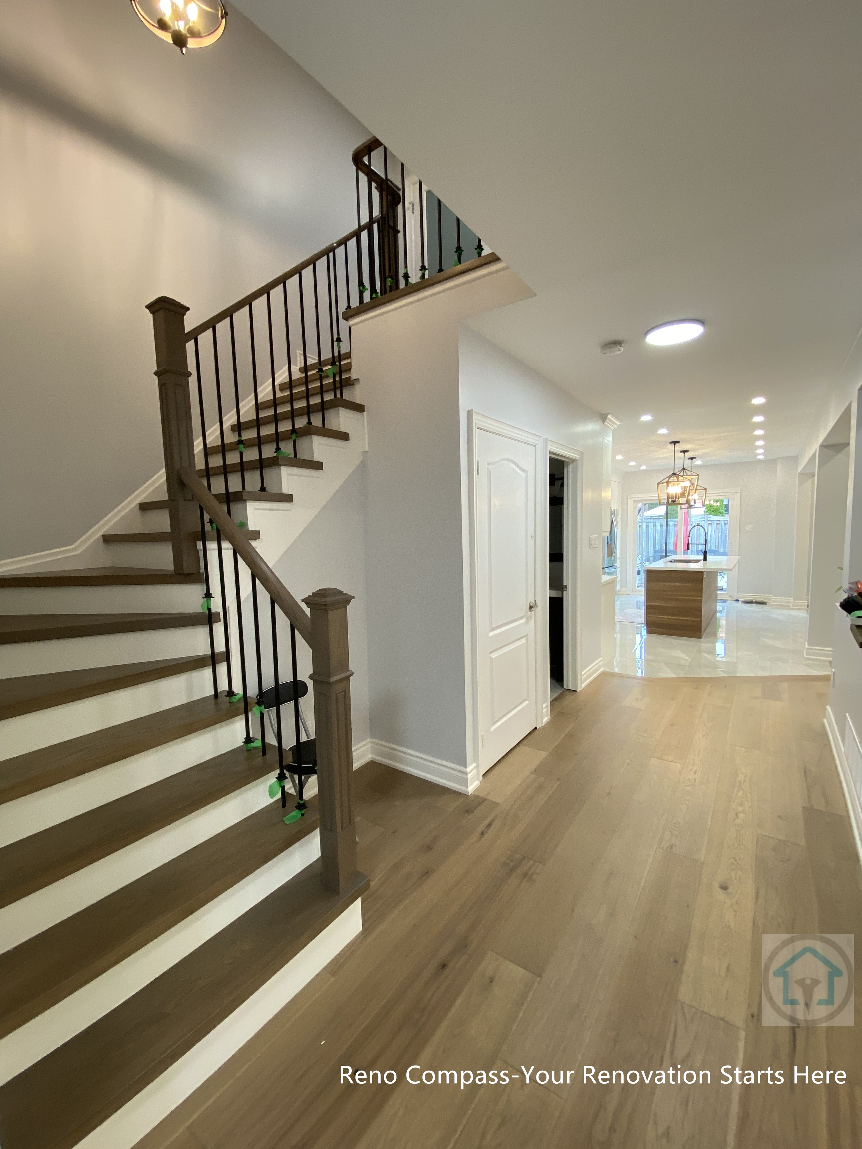 This image highlights a Newmarket interior renovation featuring a modern staircase seamlessly connected to the main hallway. The staircase combines warm-toned wood treads with dark metal balusters, creating a clean and timeless look that balances structure and elegance. Continuous hardwood flooring extends from the hallway into adjacent living areas, enhancing visual flow and spatial continuity. Recessed ceiling lights provide consistent illumination, guiding movement through the home while maintaining a bright and open atmosphere. Neutral wall finishes and simple trim details reinforce the home’s modern aesthetic. Completed by a Toronto renovation company, this staircase renovation demonstrates thoughtful circulation planning, durable material selection, and a cohesive interior layout designed for long-term everyday living.