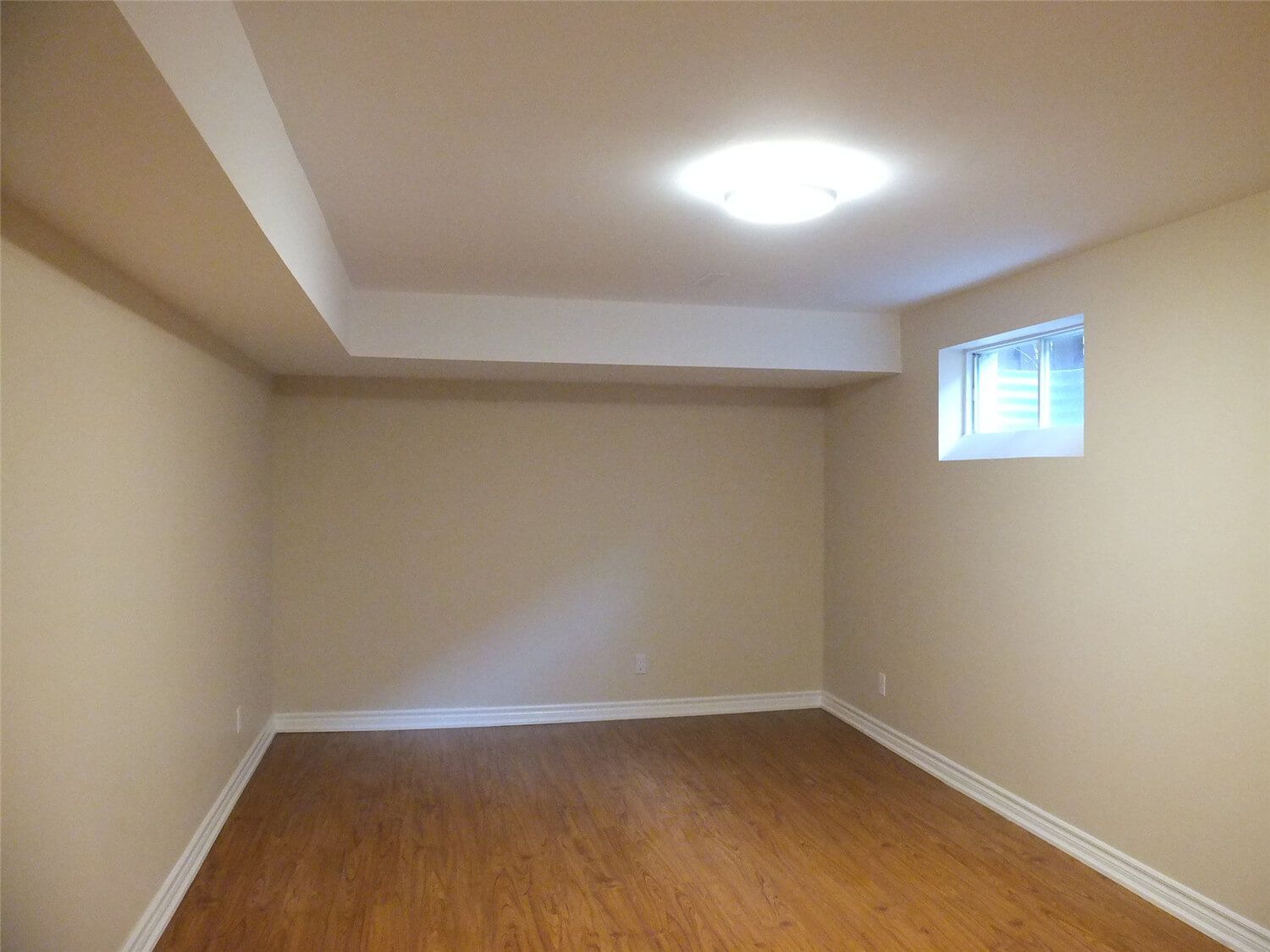 This Markham basement renovation project features newly finished walls, fresh interior painting, and durable laminate flooring installation. The clean wall finish, neutral paint tones, and wood-style flooring create a bright, comfortable living space suitable for a family recreation room or additional living area. Careful detailing around the baseboards and wall edges ensures a smooth and polished appearance throughout the basement interior.