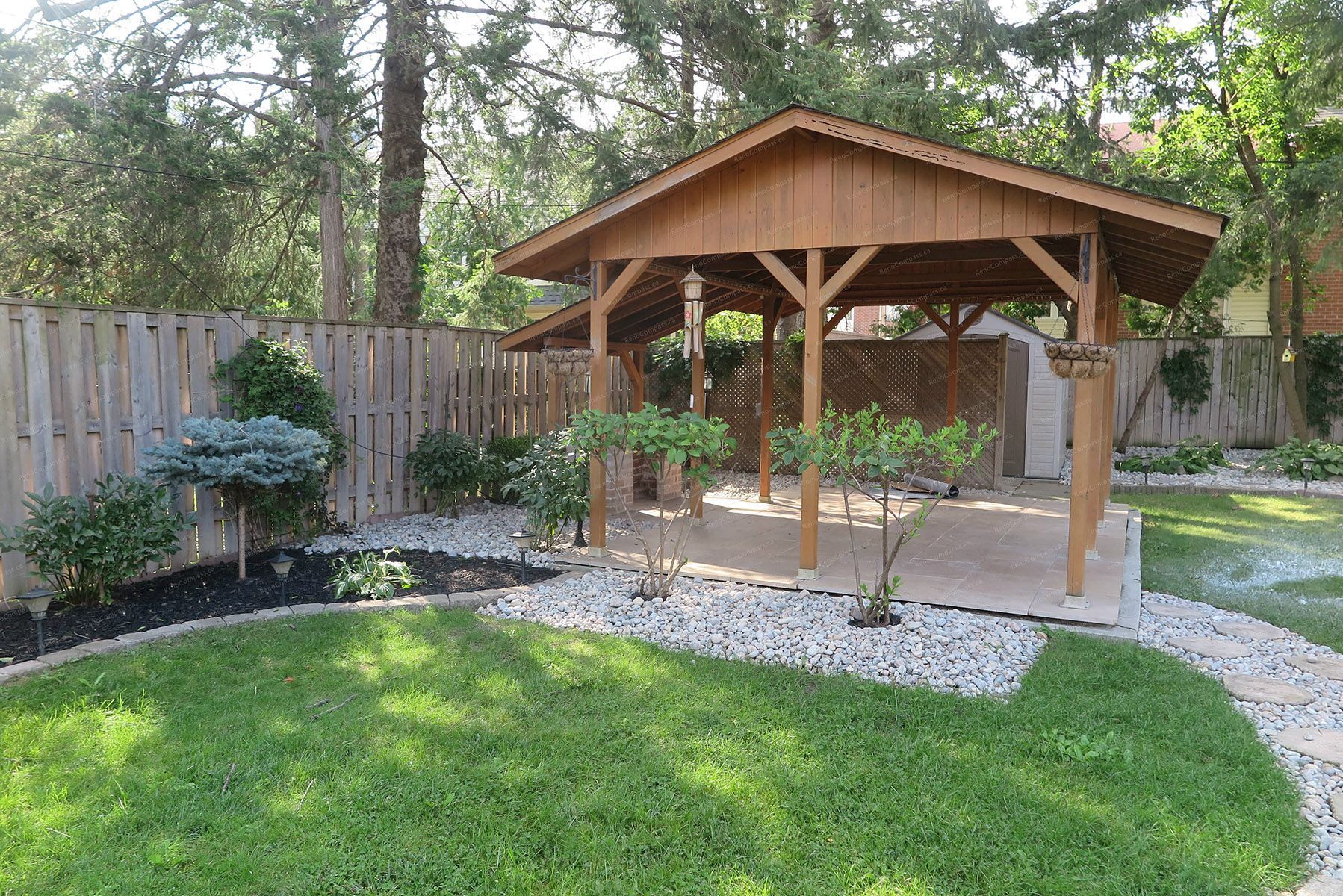 Beautiful North York outdoor landscaping project featuring a custom wooden garden pavilion, curved natural stone walkway, interlock retaining wall, and lush green lawn. Designed and built by Reno Compass to create a relaxing and functional backyard retreat with elegant garden structure and professional landscaping layout.
