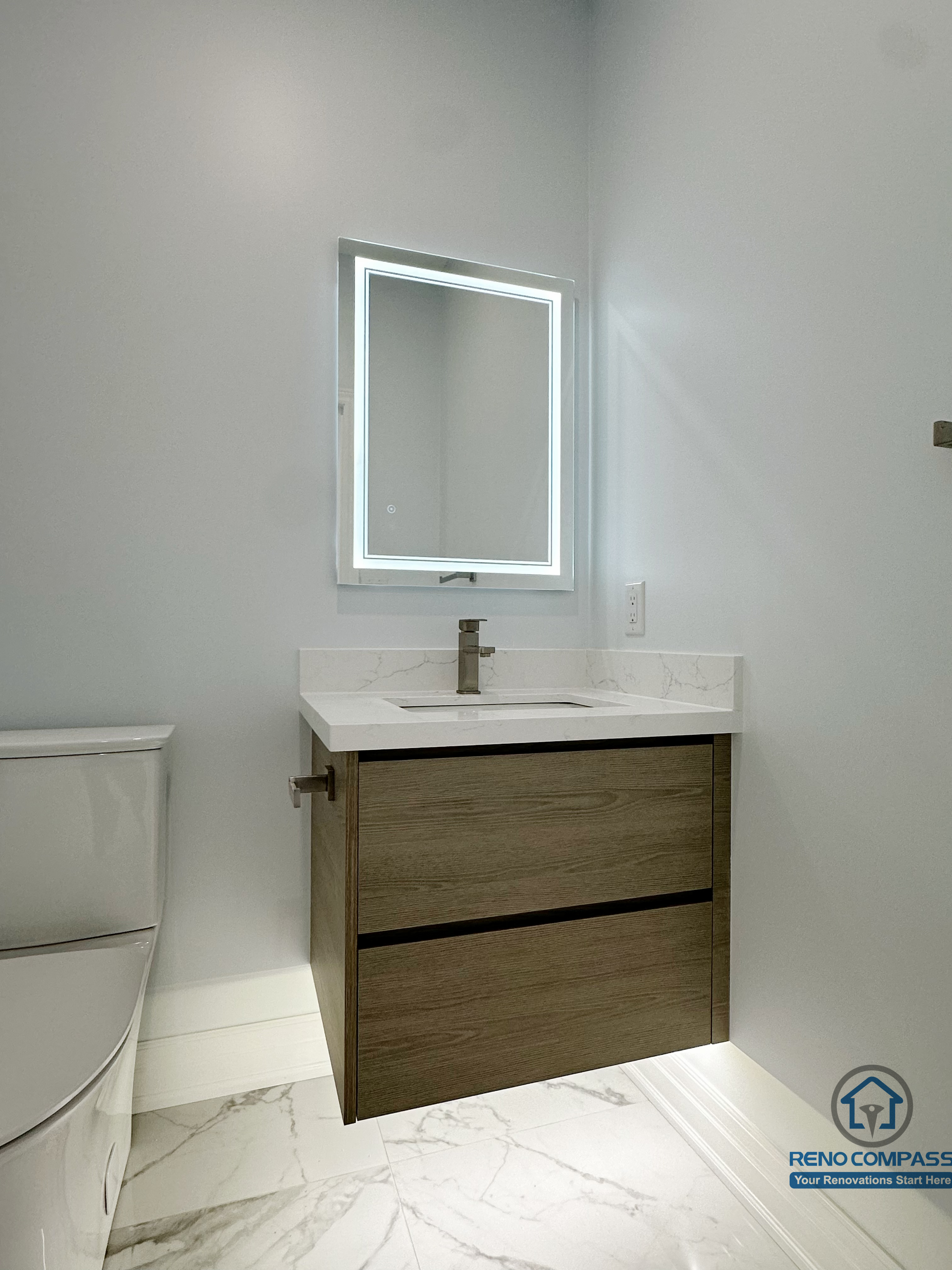 This image shows a compact bathroom renovation in a Markham house, featuring a floating wood vanity with clean-lined drawers, a marble-look countertop, and a square LED backlit mirror. The wall-mounted design improves visual openness while maintaining practical storage, making it ideal for a secondary bathroom or powder room with a modern, minimalist aesthetic.