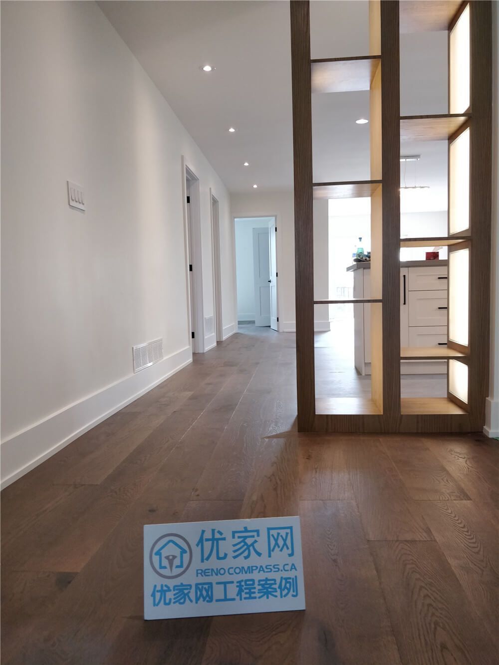This North York interior renovation showcases an open-concept hallway finished with wide-plank wood flooring, recessed ceiling lighting, and a custom wood divider that subtly separates the living space from the kitchen. The design enhances visual flow while maintaining functional zoning and a clean, modern aesthetic.