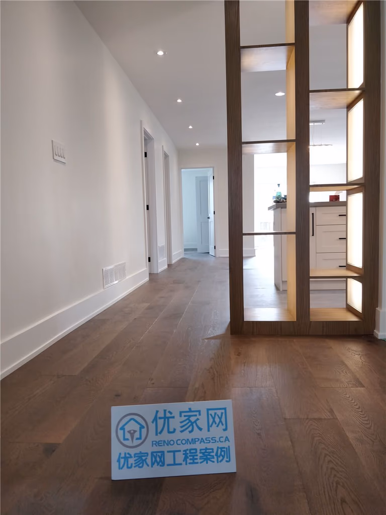 This North York interior renovation showcases an open-concept hallway finished with wide-plank wood flooring, recessed ceiling lighting, and a custom wood divider that subtly separates the living space from the kitchen. The design enhances visual flow while maintaining functional zoning and a clean, modern aesthetic.