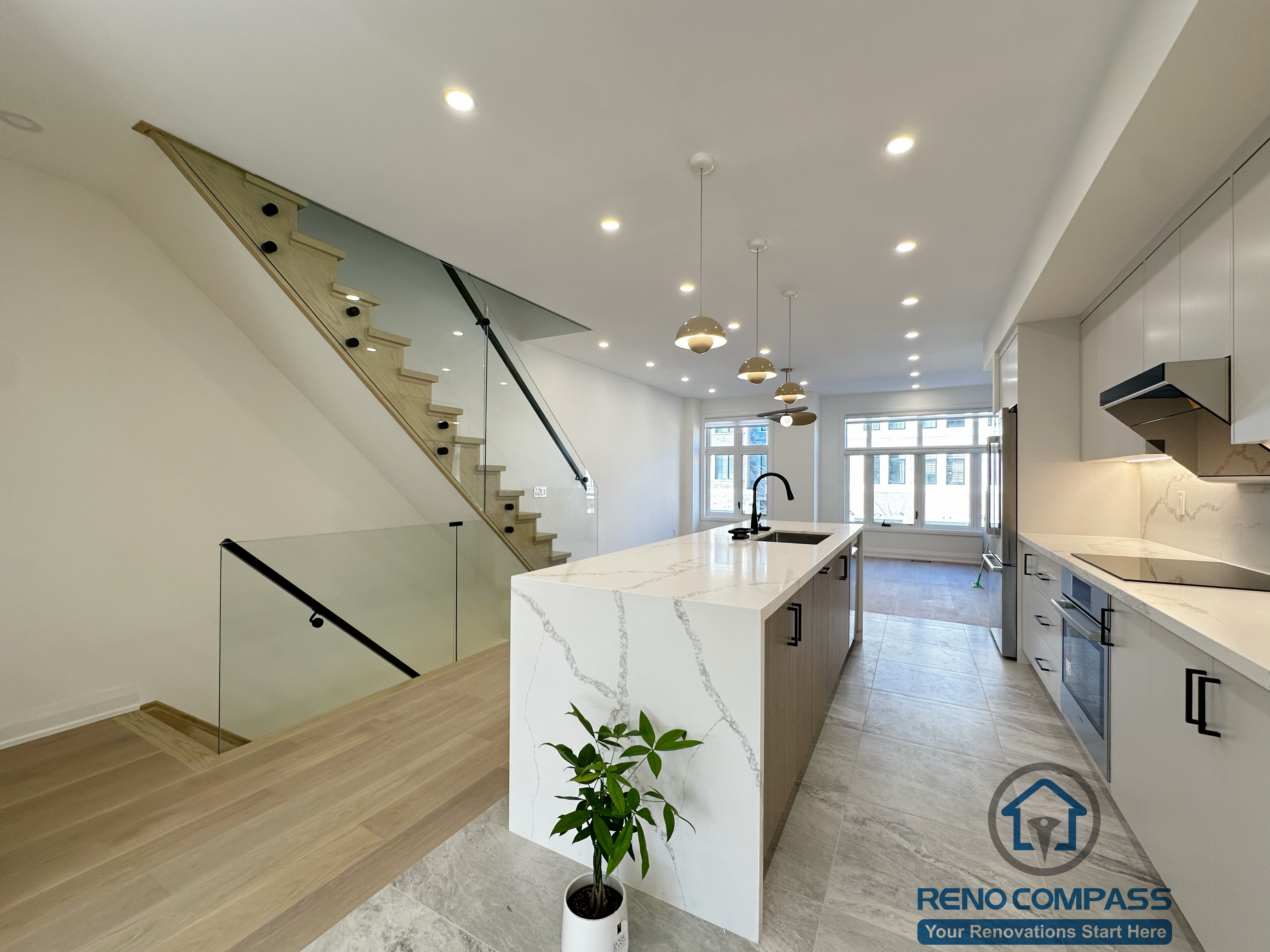 This image showcases a modern open-concept kitchen renovation in Richmond Hill, featuring a large waterfall island, custom cabinetry, built-in appliances, and warm wood flooring. The seamless layout connects the kitchen with the living area and staircase, enhancing natural light, functionality, and contemporary interior flow.