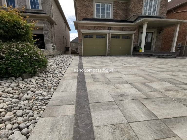 Modern interlocking driveway in Vaughan featuring elegant grey pavers, dark stone border trim, and a low-maintenance river rock side garden. Designed and installed by Reno Compass to enhance both curb appeal and drainage efficiency.