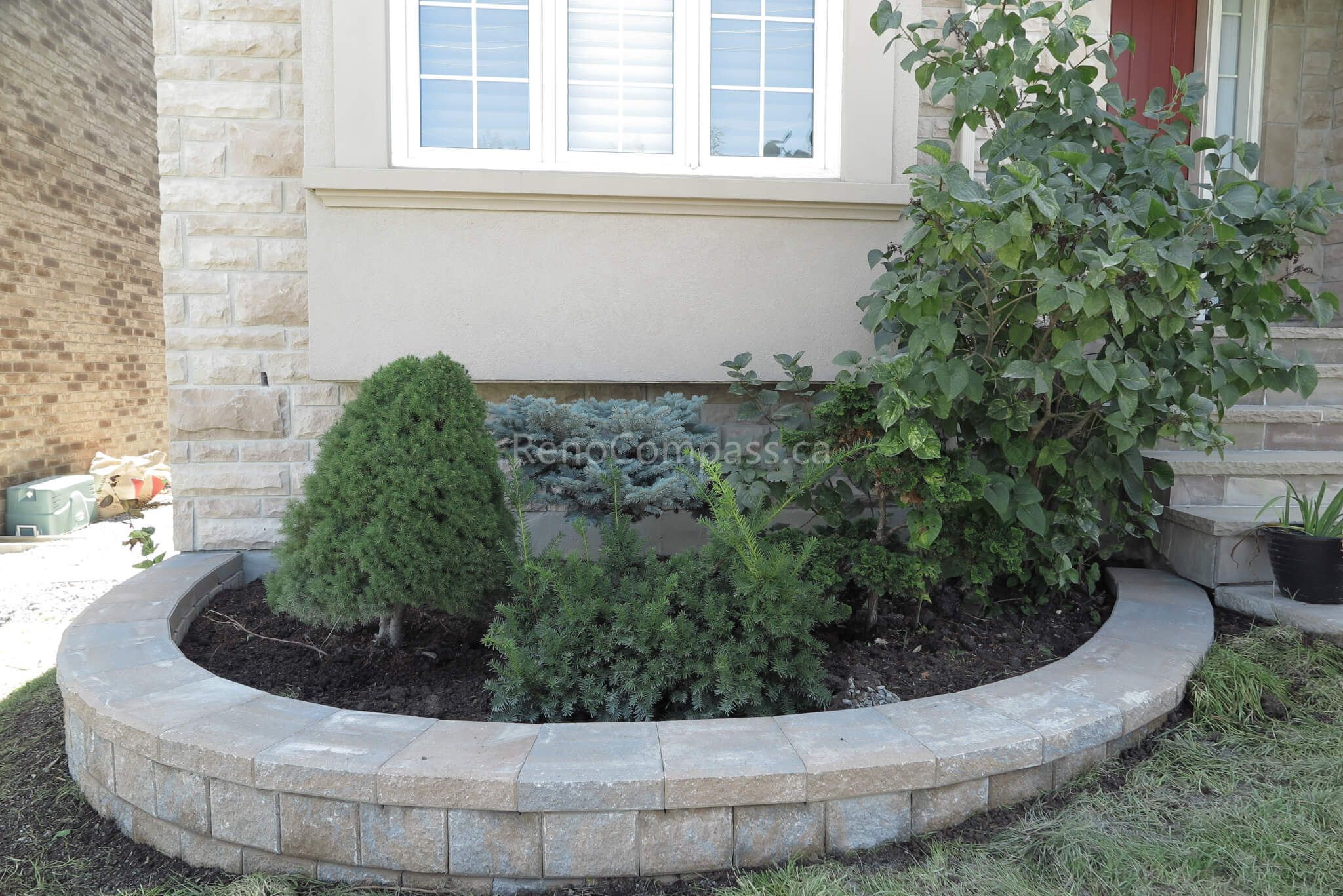 This Markham front yard landscaping project features a custom curved stone garden bed built with durable interlock retaining wall blocks and filled with fresh soil and greenery. The elegant raised planter enhances curb appeal while creating a clean, organized landscape design around the home’s exterior. Carefully installed for both structure and aesthetics, the garden bed adds depth, texture, and long-term value to the property. Completed by Reno Compass, this project delivers a refined and low-maintenance front yard landscaping solution for modern suburban homes.