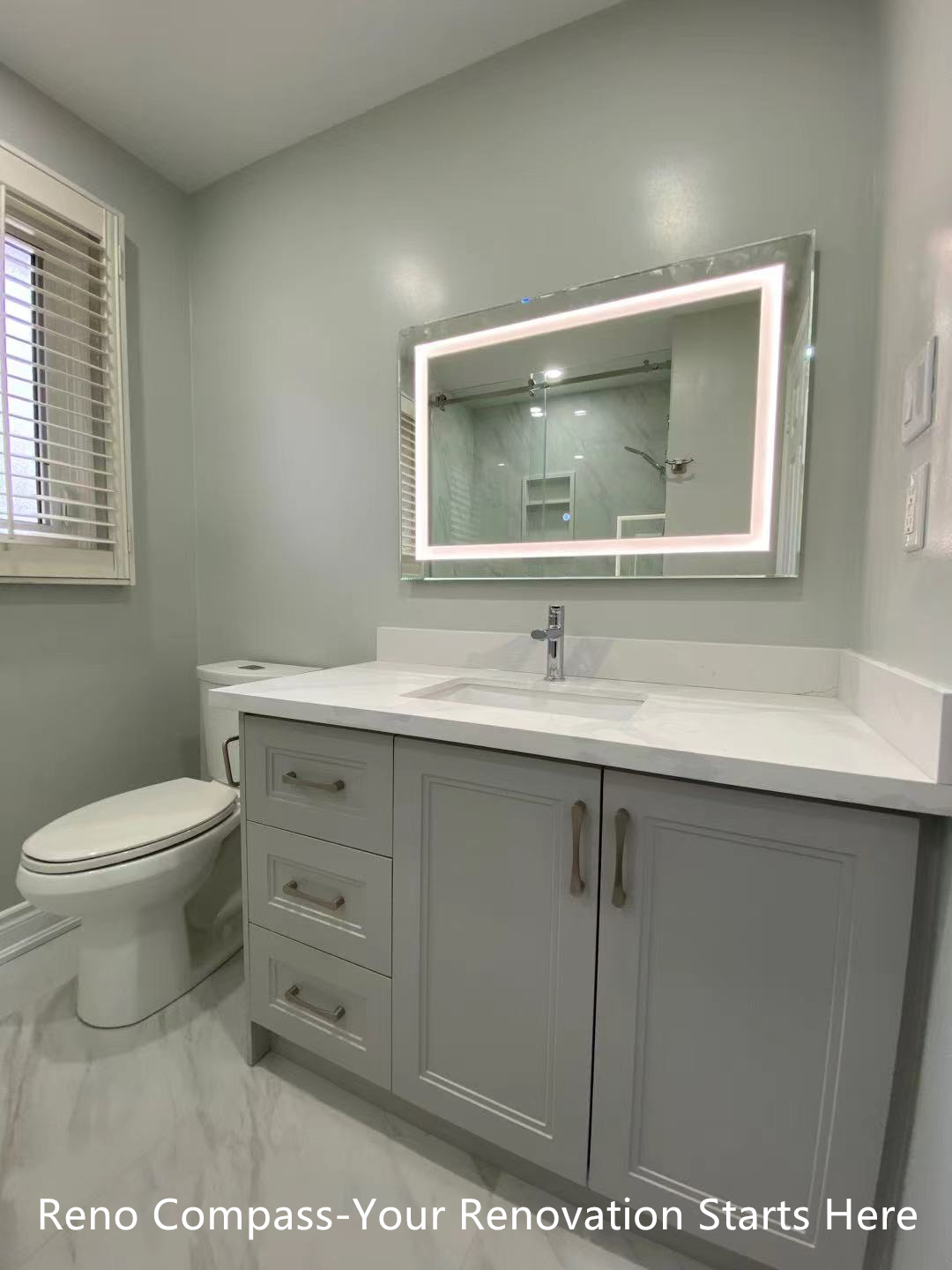 This Oakville interior renovation showcases a modern bathroom vanity designed for both functionality and clean aesthetics. The custom grey shaker-style vanity provides ample storage, paired with a quartz countertop for durability and easy maintenance. An LED backlit mirror enhances visibility while adding a contemporary touch to the space. Neutral wall tones and large-format floor tiles contribute to a bright, calm atmosphere, making the bathroom feel spacious and comfortable. This design emphasizes practical daily use while reflecting the quality craftsmanship and refined detailing delivered by a professional Toronto renovation company.