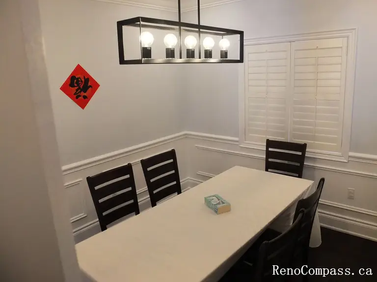 This Newmarket interior renovation features a clean and elegant dining room designed with classic wall wainscoting and rich dark hardwood flooring. Plantation shutters allow natural light to brighten the space while maintaining privacy, and the modern rectangular pendant light provides balanced illumination above the dining table. The simple layout and refined finishes create a comfortable setting for family meals and gatherings. Completed by Reno Compass Inc., this project highlights timeless interior design and high-quality craftsmanship for modern homes.