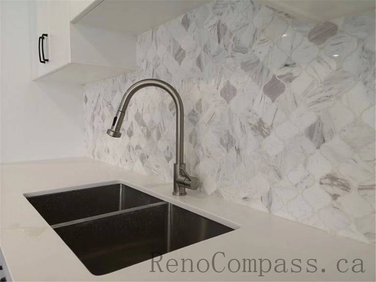 This elegant kitchen renovation in Aurora features a sleek stainless-steel faucet, a dual-basin sink, and a white marble backsplash for a polished, modern look. Designed and completed by Reno　Compass.