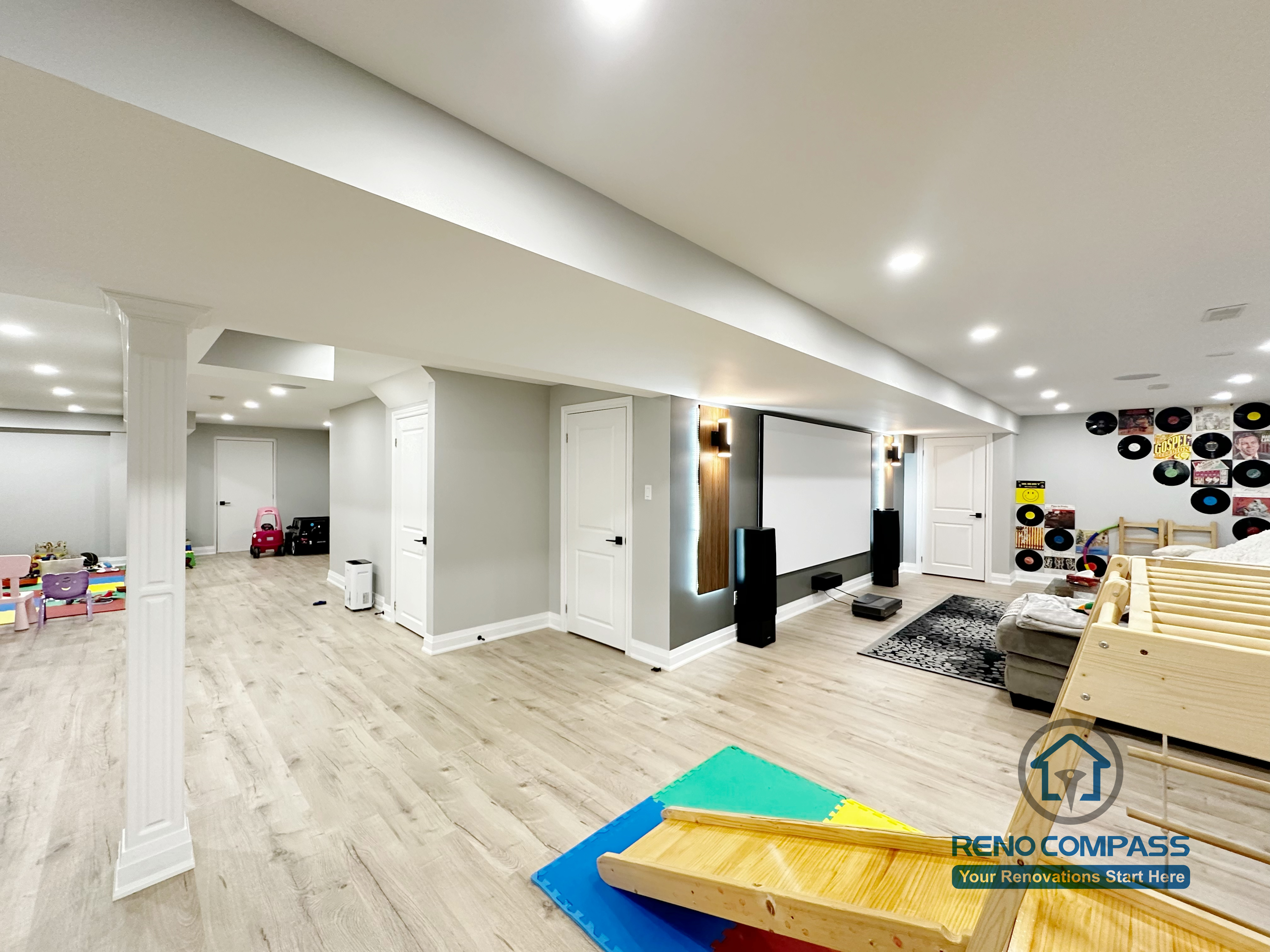 This Newmarket basement renovation highlights a spacious open-concept layout designed for family living and entertainment. The finished basement features recessed ceiling lighting, clean column detailing, durable wood-look flooring, and a seamless flow between the home theater area and children’s play space, creating a bright and highly functional lower level.