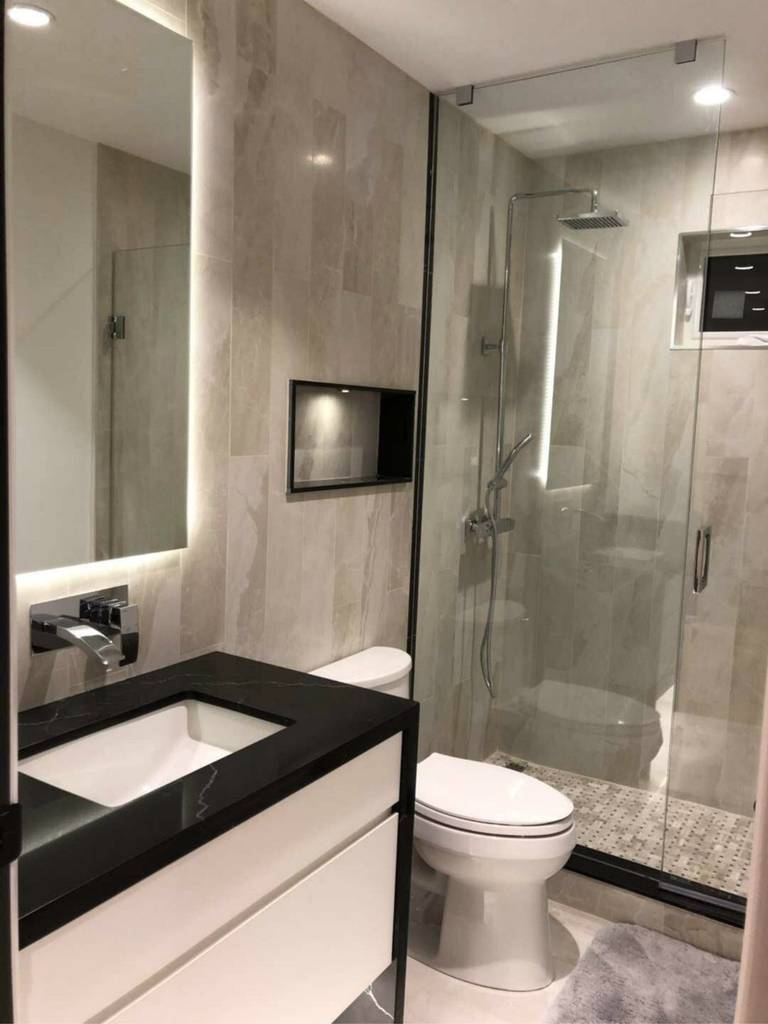 Contemporary bathroom renovation in Markham featuring a sleek glass shower enclosure, LED backlit mirror, black quartz vanity countertop, and marble-style wall tiles. This modern bathroom design combines functionality and elegance, creating a bright and luxurious space tailored for everyday comfort and long-term home value.