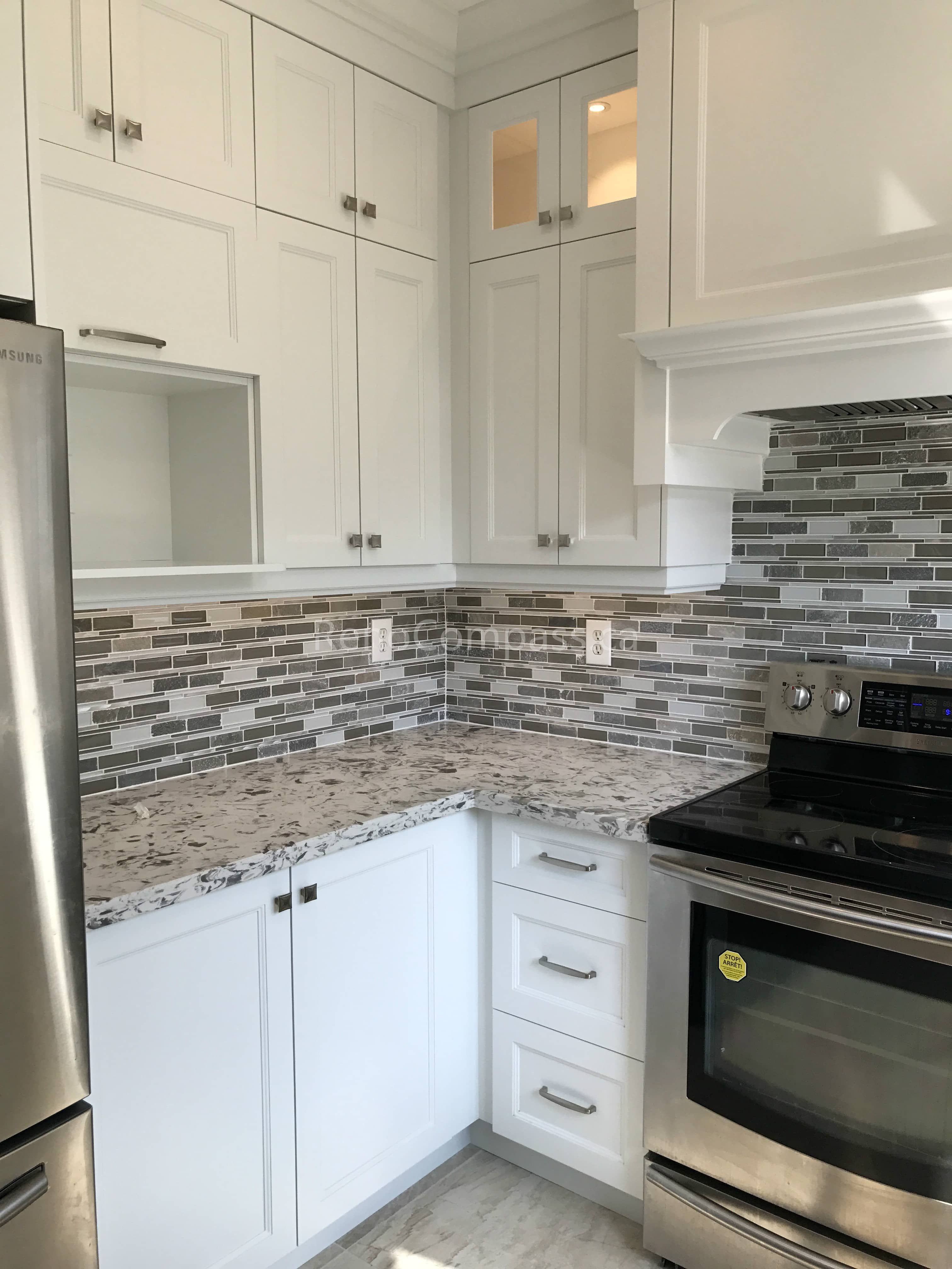This Markham kitchen renovation showcases custom white cabinetry with extended upper storage, granite countertops, and a modern mosaic tile backsplash. The redesigned corner layout maximizes functionality and storage while maintaining a clean, bright aesthetic. Stainless steel appliances and detailed millwork complete this timeless and practical kitchen upgrade.