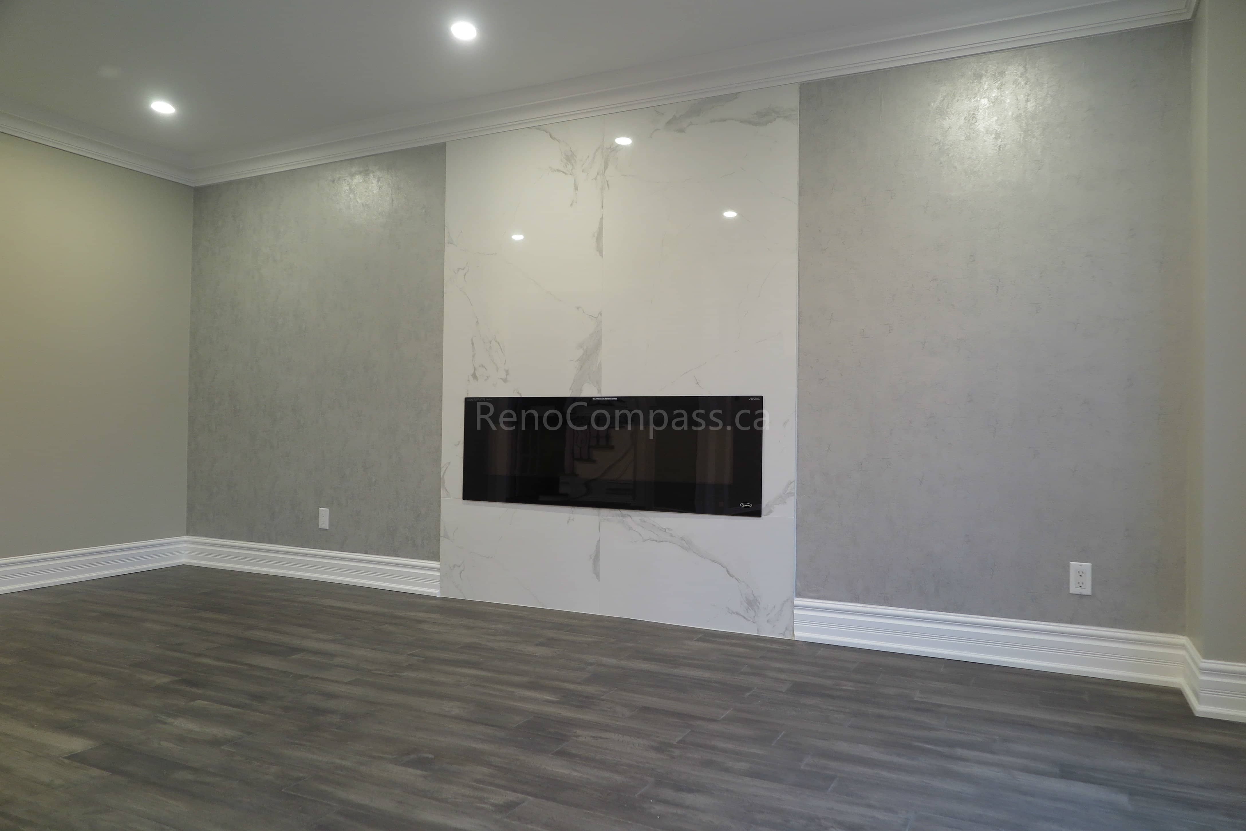 This Markham interior renovation highlights a modern living room upgrade featuring a sleek built-in linear fireplace and a marble-style feature wall. The space is finished with warm neutral paint tones, crown molding details, and newly installed dark hardwood flooring, creating a clean and elegant contemporary atmosphere. Completed by Reno Compass, a trusted renovation contractor providing professional interior renovation and custom finishing services in Markham and the Greater Toronto Area.