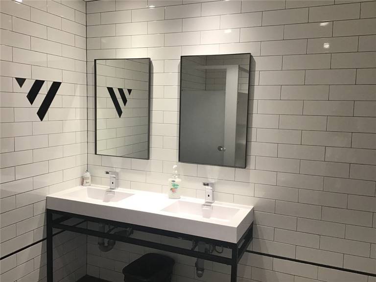 Modern commercial washroom renovation in downtown Toronto featuring double vanity sinks, white subway tile walls, black metal framing, and clean functional design ideal for office or retail spaces.