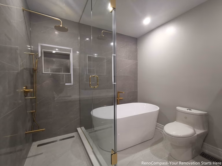 This Oakville master bathroom full renovation features a modern walk-in glass shower, freestanding bathtub, and sleek contemporary layout designed for comfort and luxury. Large-format marble-style tiles, premium gold fixtures, recessed shower niche, and linear drain create a clean, spa-inspired atmosphere. The combination of frameless glass enclosure, modern toilet installation, and bright lighting enhances both functionality and visual space. Completed by a trusted Toronto renovation company, this bathroom upgrade delivers long-lasting quality, elegant design, and increased property value for the homeowner.