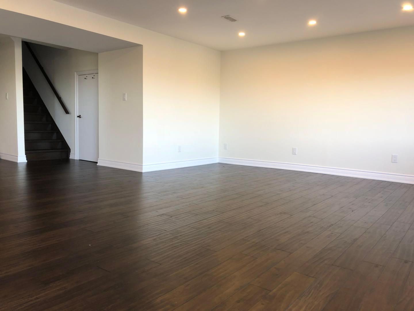 Fully finished lower-level space in a Toronto basement renovation, showcasing seamless hardwood flooring, recessed ceiling lighting, smooth wall finishes, and integrated stair access connecting the main floor to the newly renovated basement living area.
