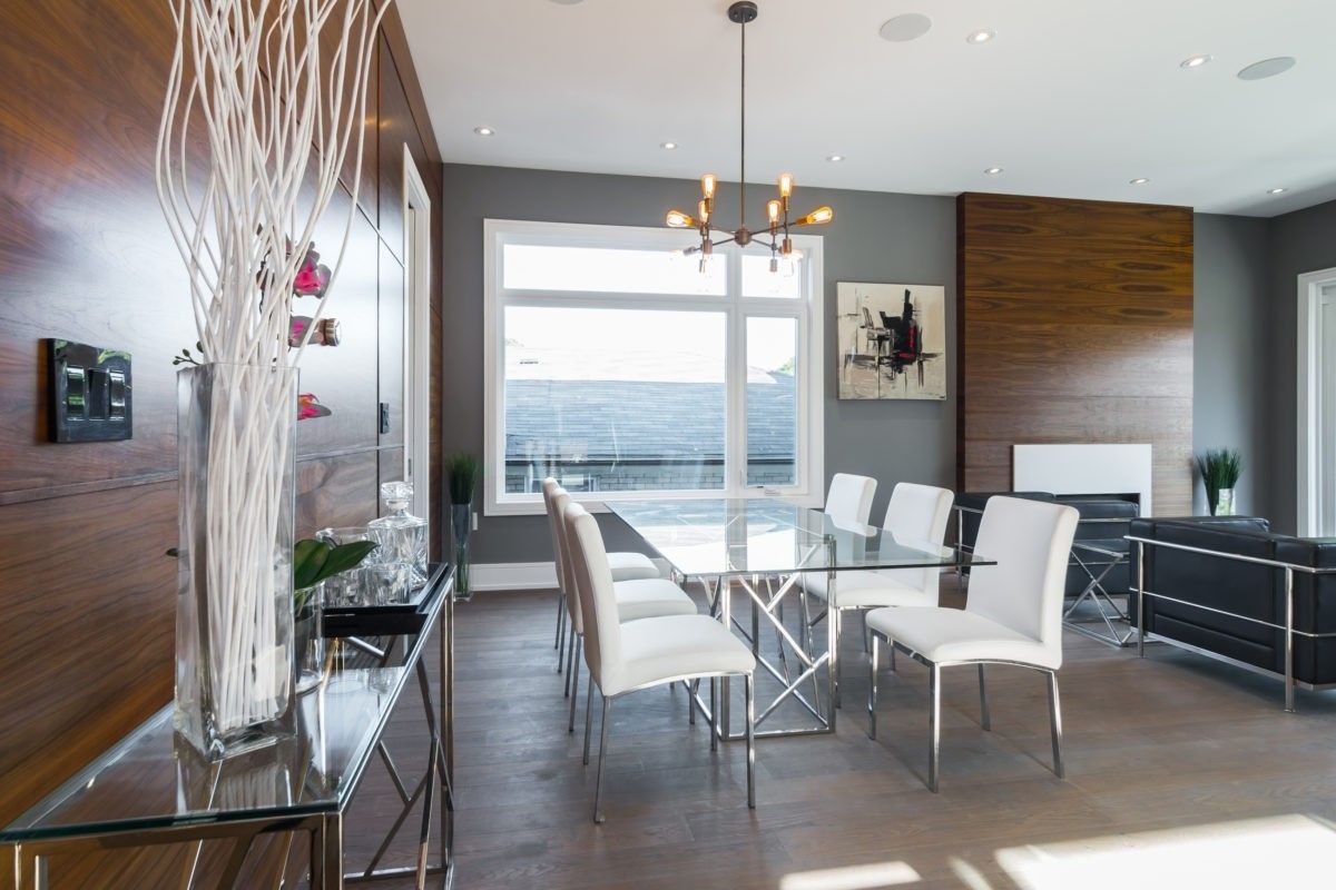 This Toronto modern interior renovation features a bright and elegant dining area with an open-concept layout, floor-to-ceiling windows, and a sleek glass dining table. The space is enhanced by rich wood accent walls, contemporary lighting fixtures, and natural light, creating a refined environment perfect for gatherings and everyday dining.