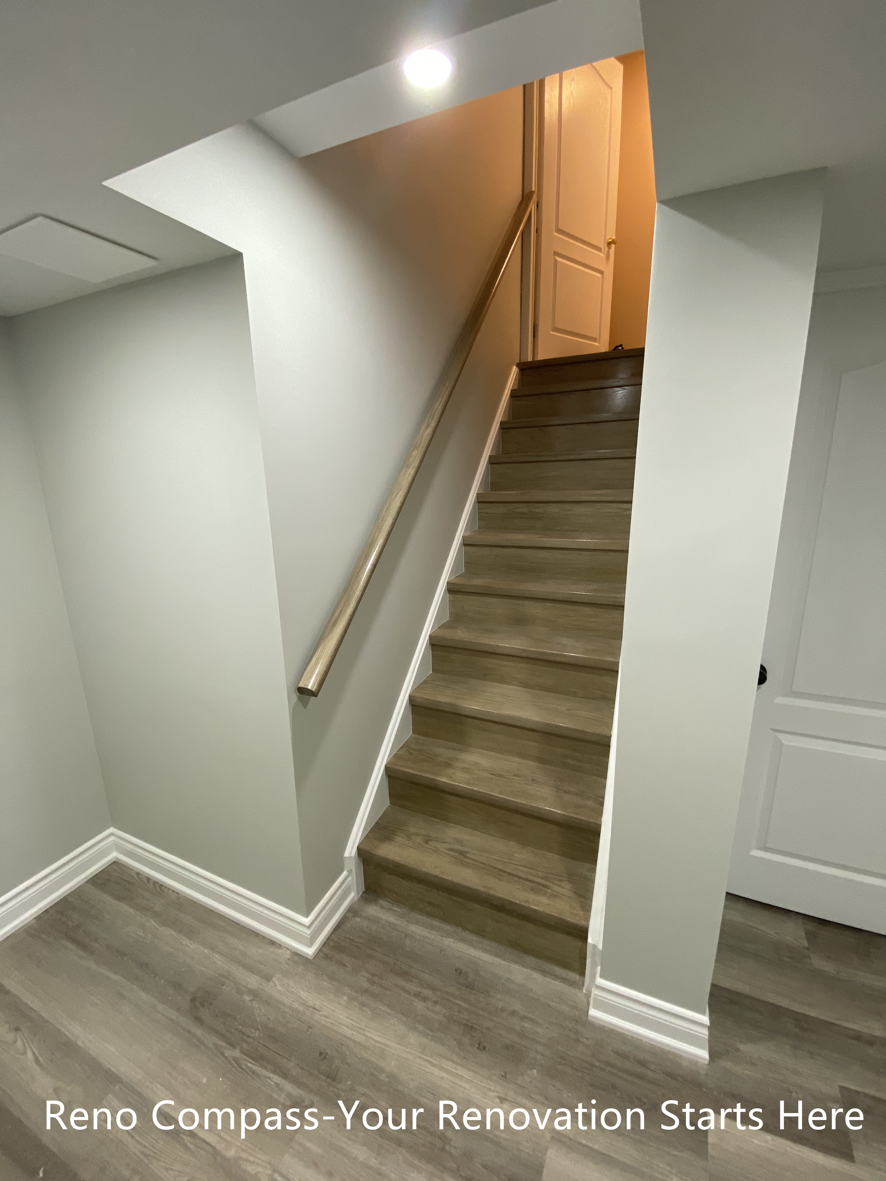 This image highlights the renovated basement staircase connecting the lower level to the main floor in this Aurora home. The staircase was refinished with durable, wood-look steps and clean white trim to create a cohesive transition between levels. Neutral wall colors and a streamlined handrail help keep the stairwell visually open while improving safety and everyday usability.

Recessed lighting was added above the stair opening to enhance visibility and reduce shadowing, making the space feel brighter and more inviting. By simplifying structural lines and finishes, the staircase integrates naturally into the overall basement layout without feeling enclosed or heavy. This renovation improves both circulation and visual continuity, supporting a clean, modern basement design.
City: Aurora | Toronto Contractor: Reno Compass
