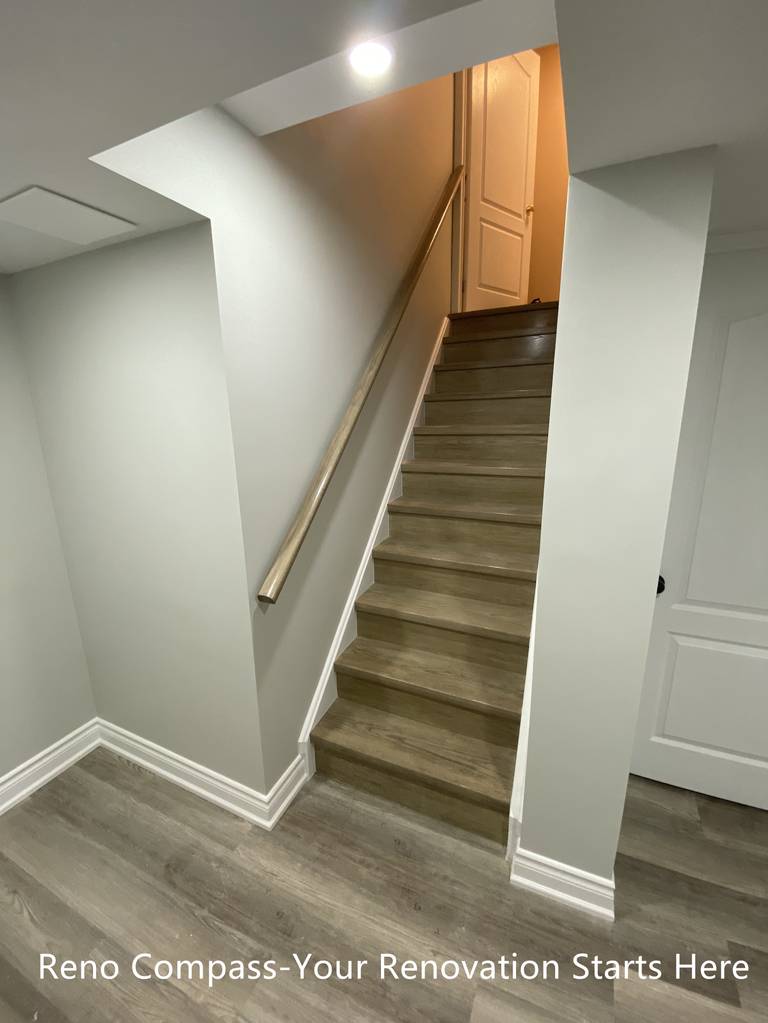 This image highlights the renovated basement staircase connecting the lower level to the main floor in this Aurora home. The staircase was refinished with durable, wood-look steps and clean white trim to create a cohesive transition between levels. Neutral wall colors and a streamlined handrail help keep the stairwell visually open while improving safety and everyday usability.

Recessed lighting was added above the stair opening to enhance visibility and reduce shadowing, making the space feel brighter and more inviting. By simplifying structural lines and finishes, the staircase integrates naturally into the overall basement layout without feeling enclosed or heavy. This renovation improves both circulation and visual continuity, supporting a clean, modern basement design.
City: Aurora | Toronto Contractor: Reno Compass