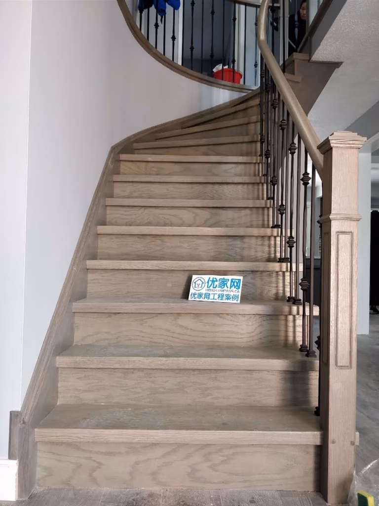 Elegant staircase renovation in Ajax featuring natural wood stair treads, curved staircase design, and modern black iron balusters. The upgrade enhances both safety and visual appeal, creating a warm and contemporary transition between floors in this residential interior renovation project completed by a professional Toronto renovation company.